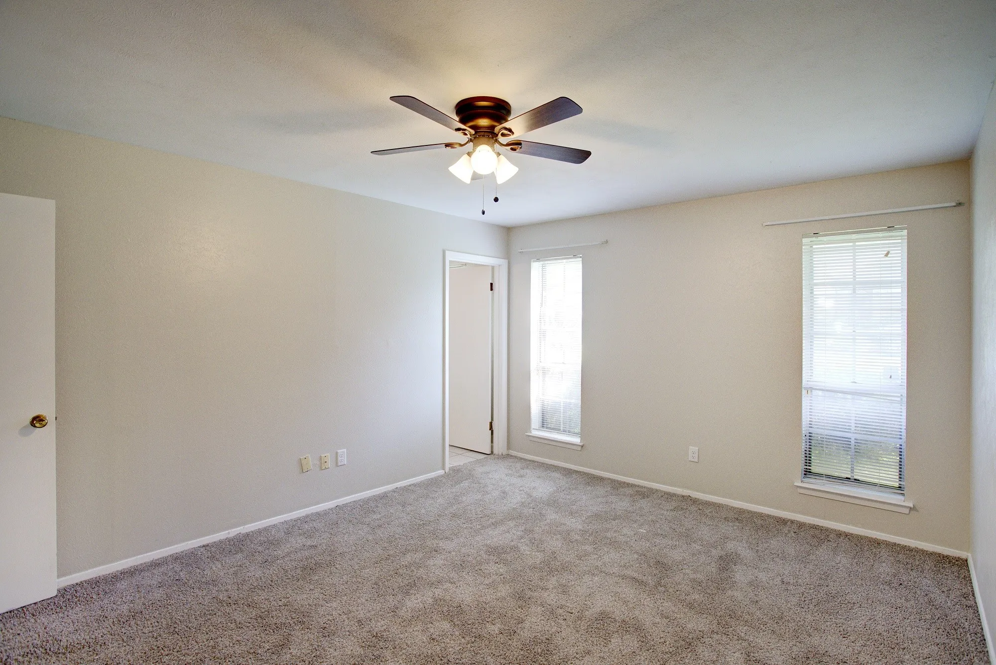 Neutral-toned walls, plush carpeting, ceiling fan with integrated lighting, and two windows