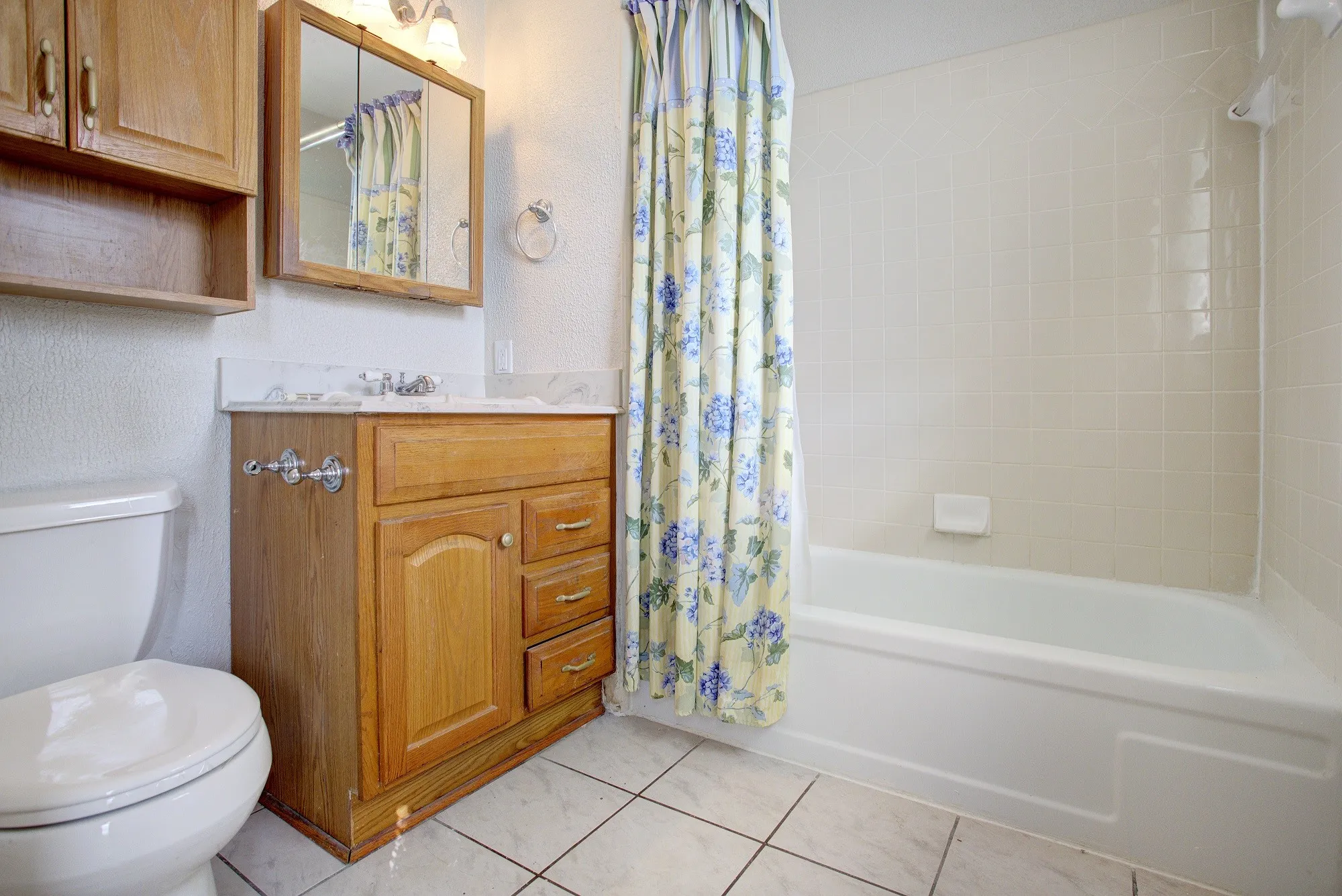 Bathroom featuring a wood-finish vanity with white countertop, integrated sink, and white ceramic tile flooring