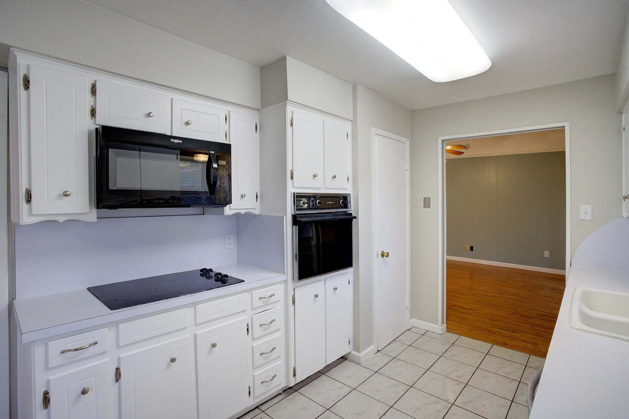 Built-in wall oven and microwave, white cabinetry with hardware, tile flooring, and integrated countertop cooktop