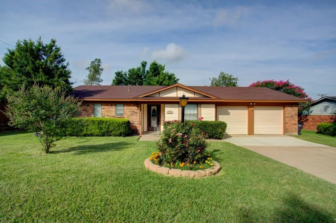 Brick facade with a brown shingle roof, two-car garage, concrete driveway, and established landscaping