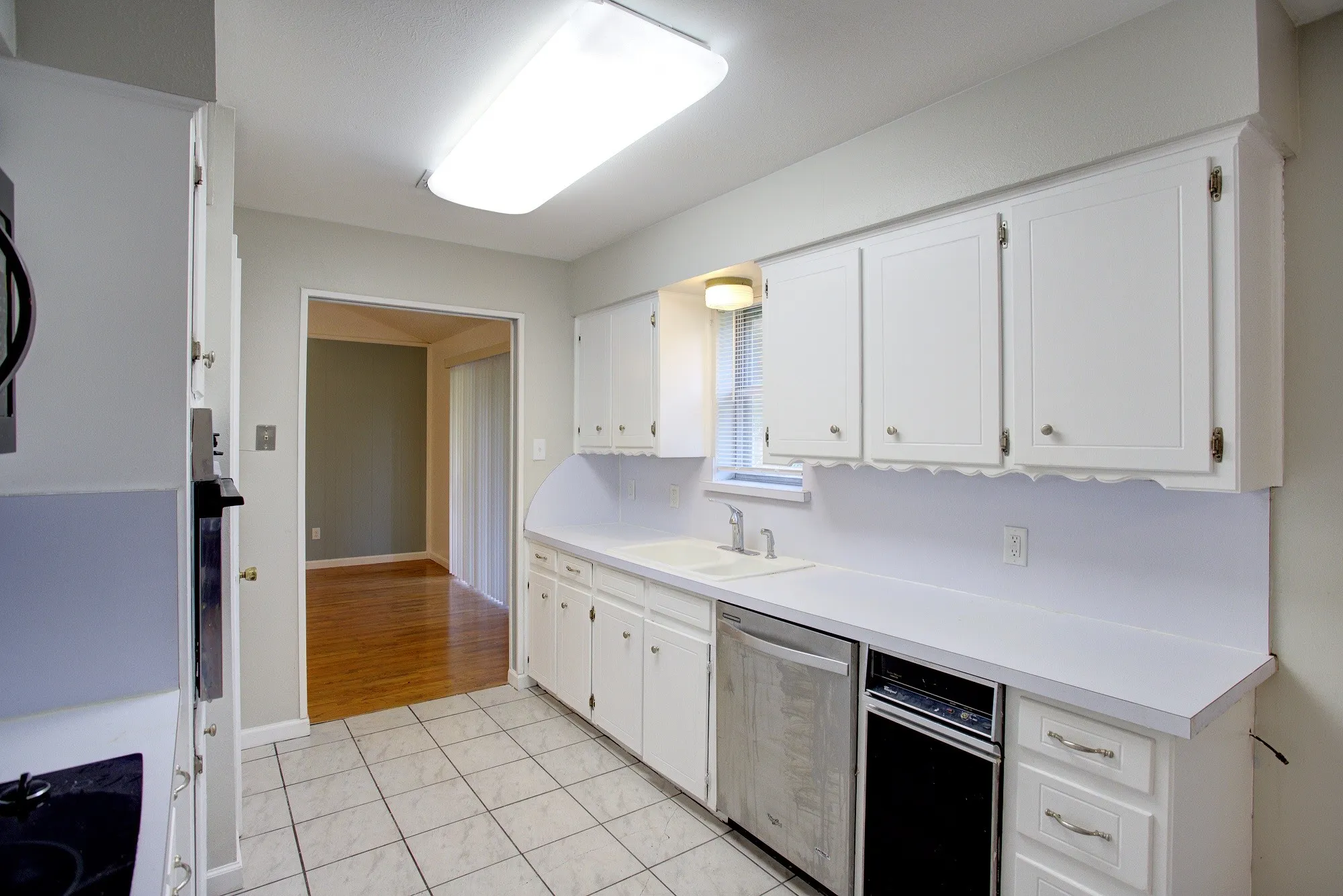White cabinetry with decorative trim, white countertops, dual basin sink, integrated dishwasher, and tile flooring
