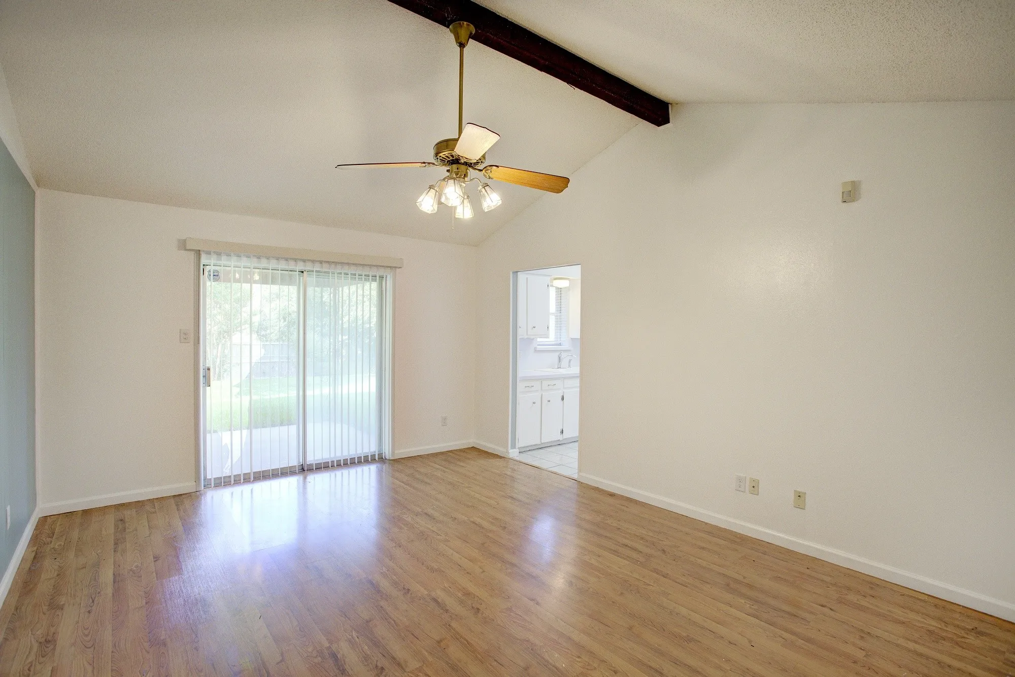 Wood-finish flooring, vaulted ceiling with exposed beam, ceiling fan with integrated lighting, and sliding glass doors to the exterior