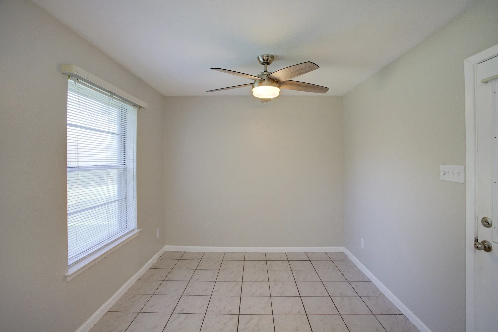 Room featuring a ceiling fan with integrated lighting, a double-hung window with blinds, and tiled flooring
