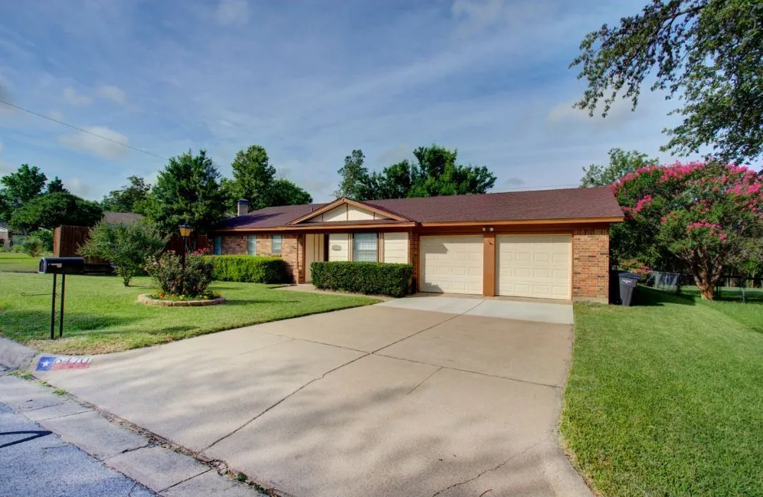 Brick exterior with a two-car garage, mature landscaping, and a concrete driveway