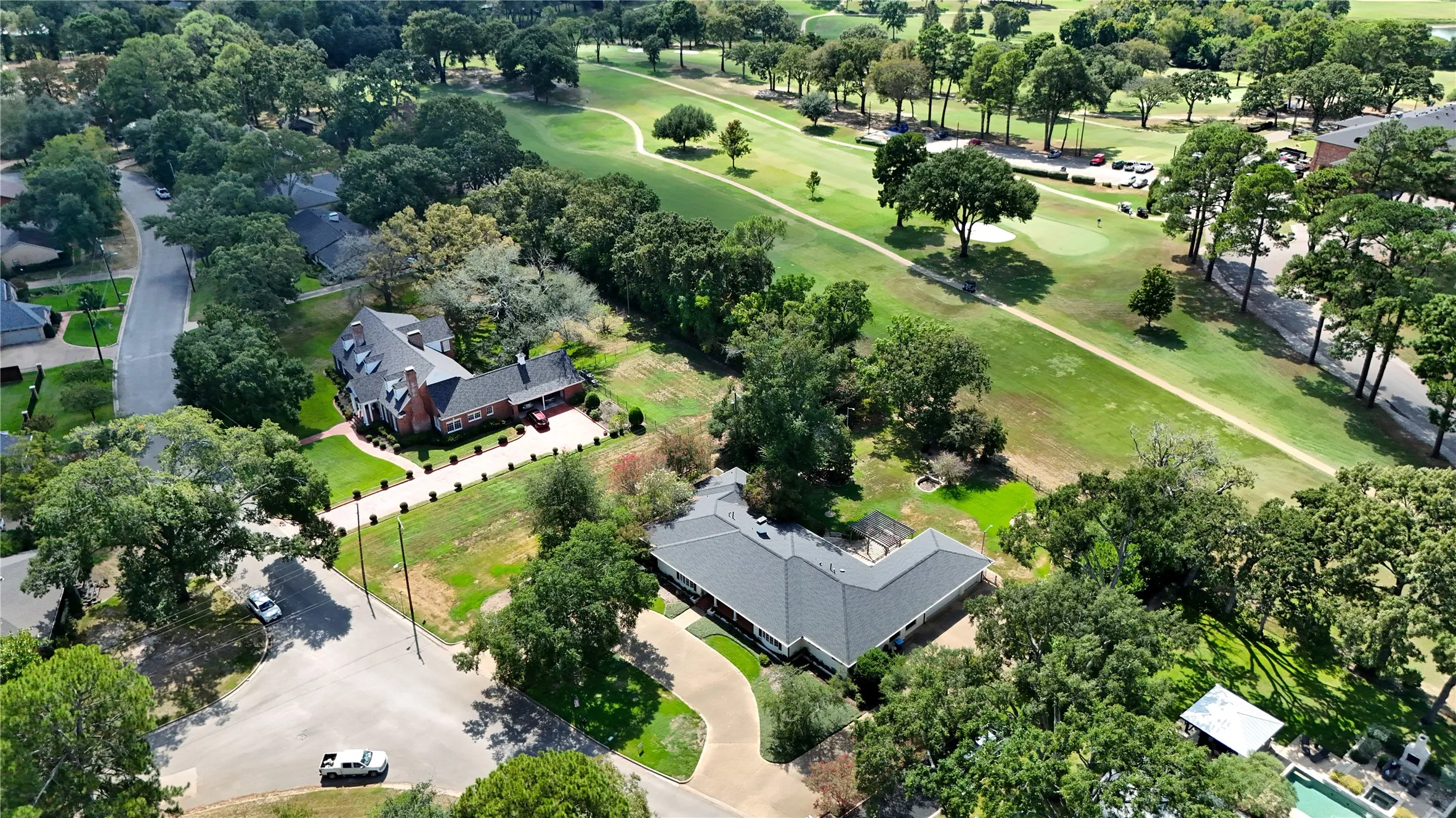 Property featuring a brick exterior, extensive green space, mature trees, and a paved driveway