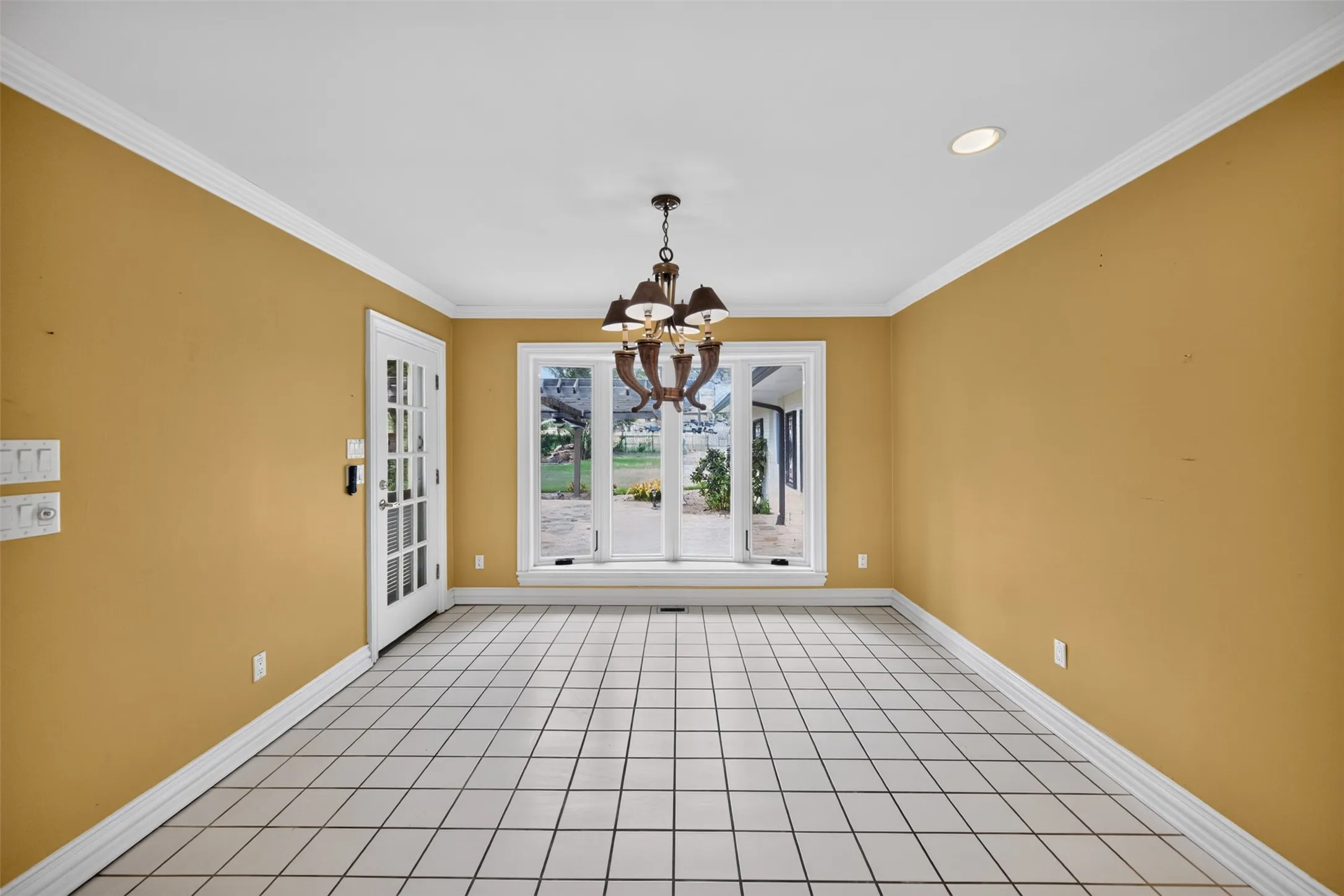 Tile flooring, crown molding, a multi-pane glass door, recessed lighting, and a chandelier