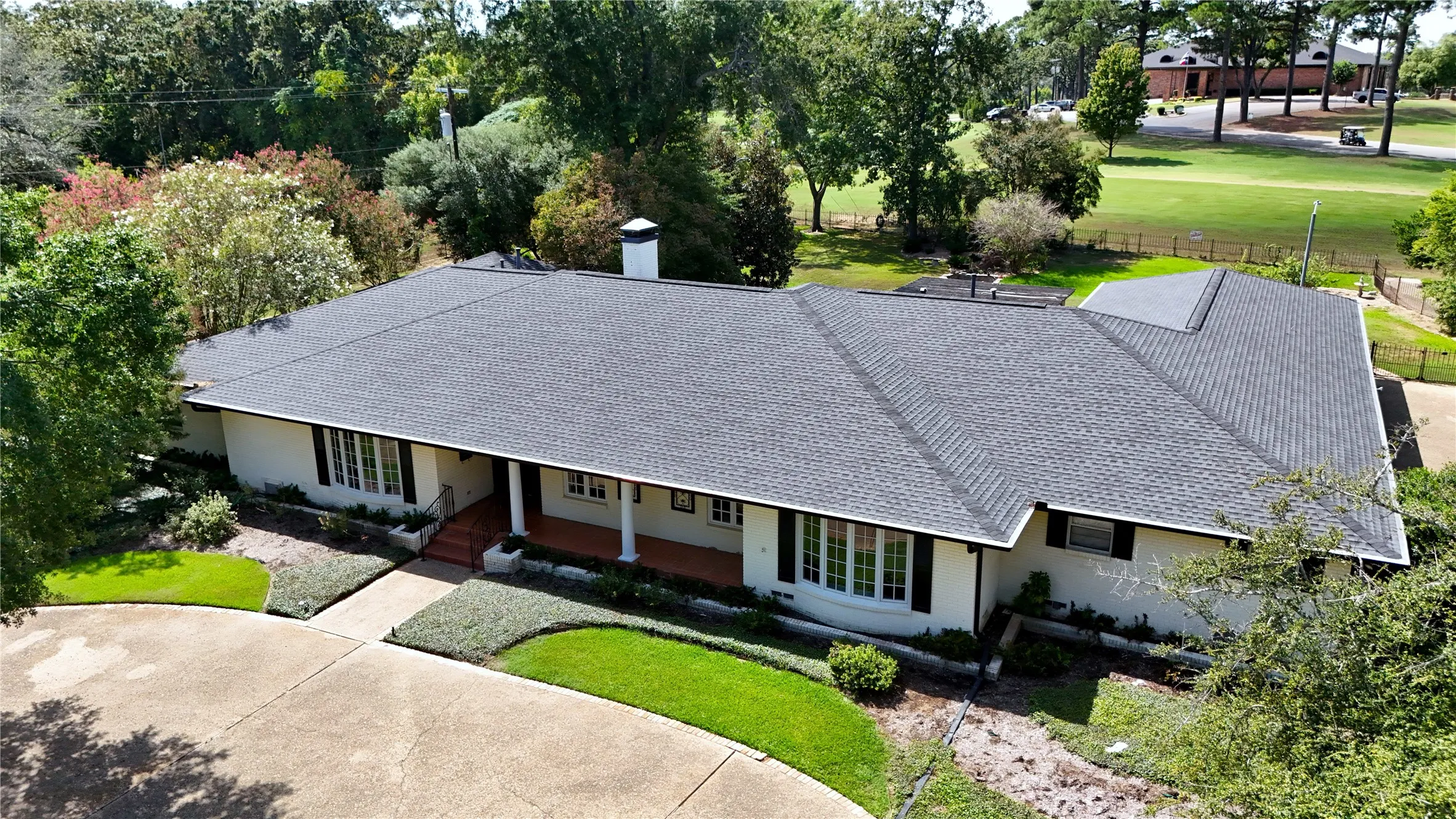 Expansive asphalt shingle roof, bay window, manicured landscaping, concrete driveway, and covered front porch with columns