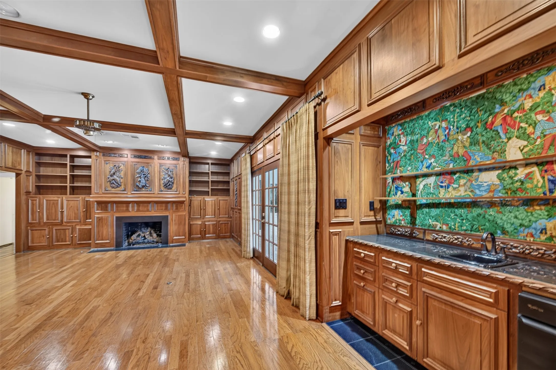 Hardwood flooring, wood-paneled walls, built-in shelving, fireplace, and a built-in wet bar with a granite countertop