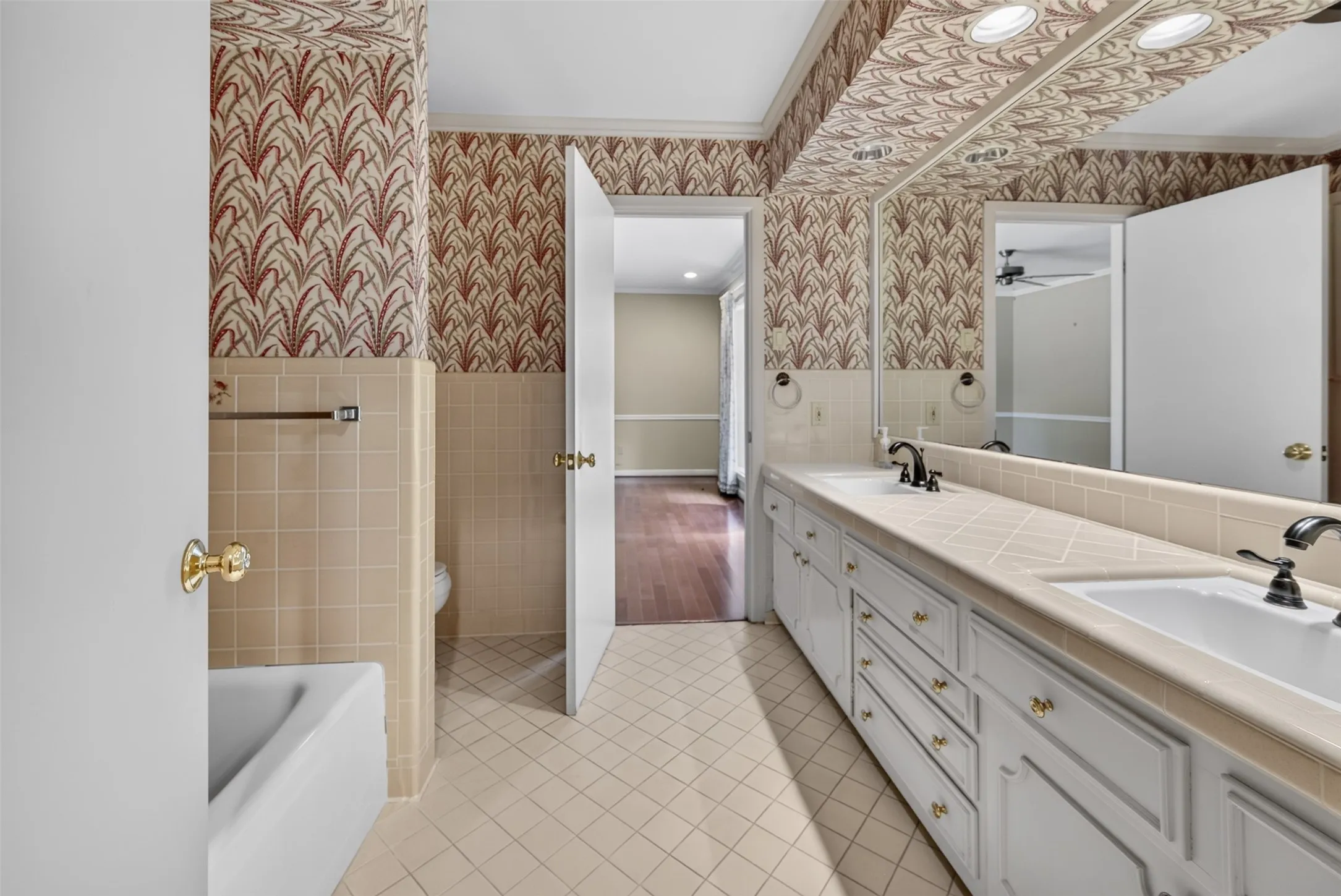 Dual vanity with integrated sinks, extensive countertop space, white cabinetry with brass-tone hardware, and a full-width mirror