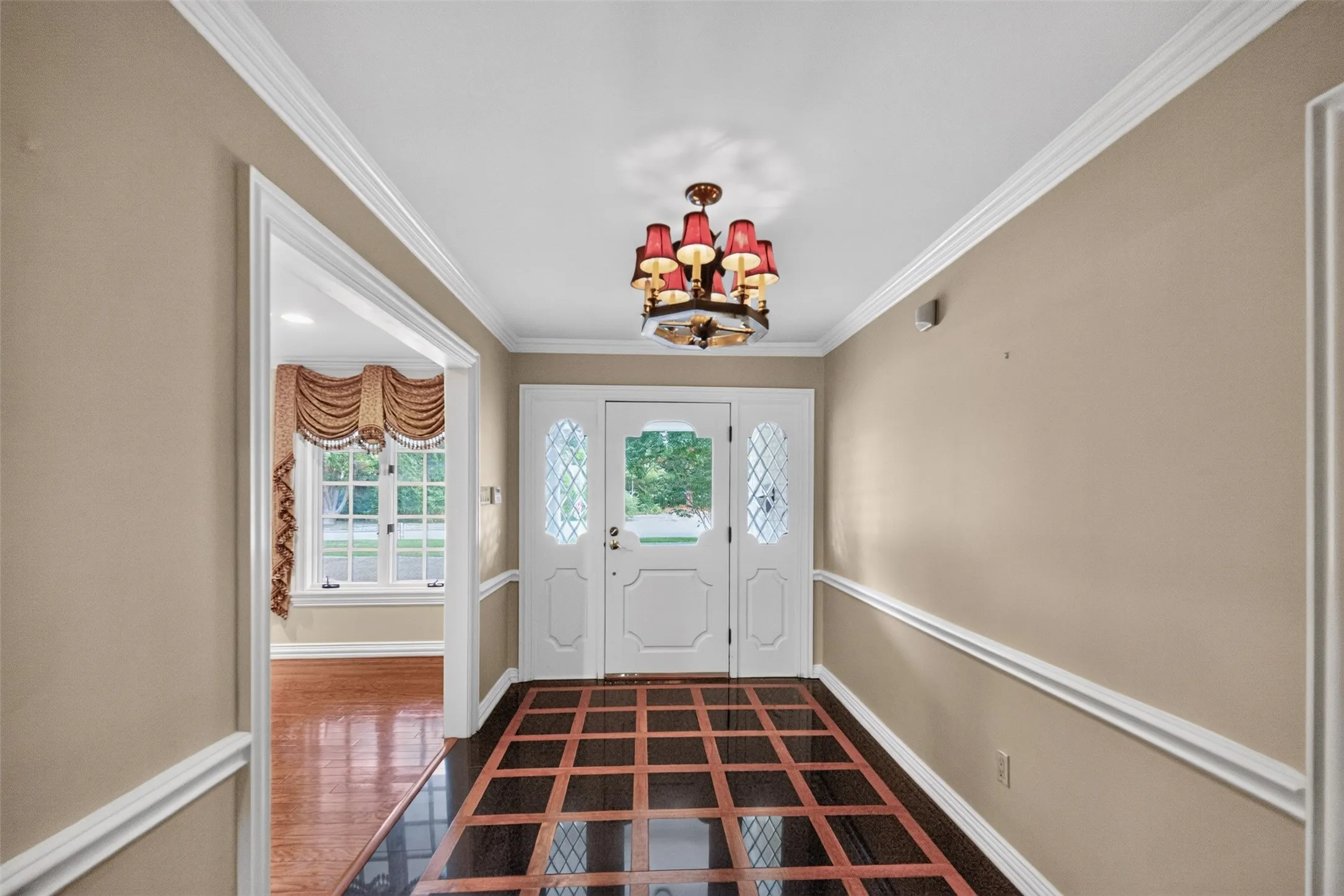 Foyer featuring a decorative chandelier, white crown molding, and a patterned wood-finish floor