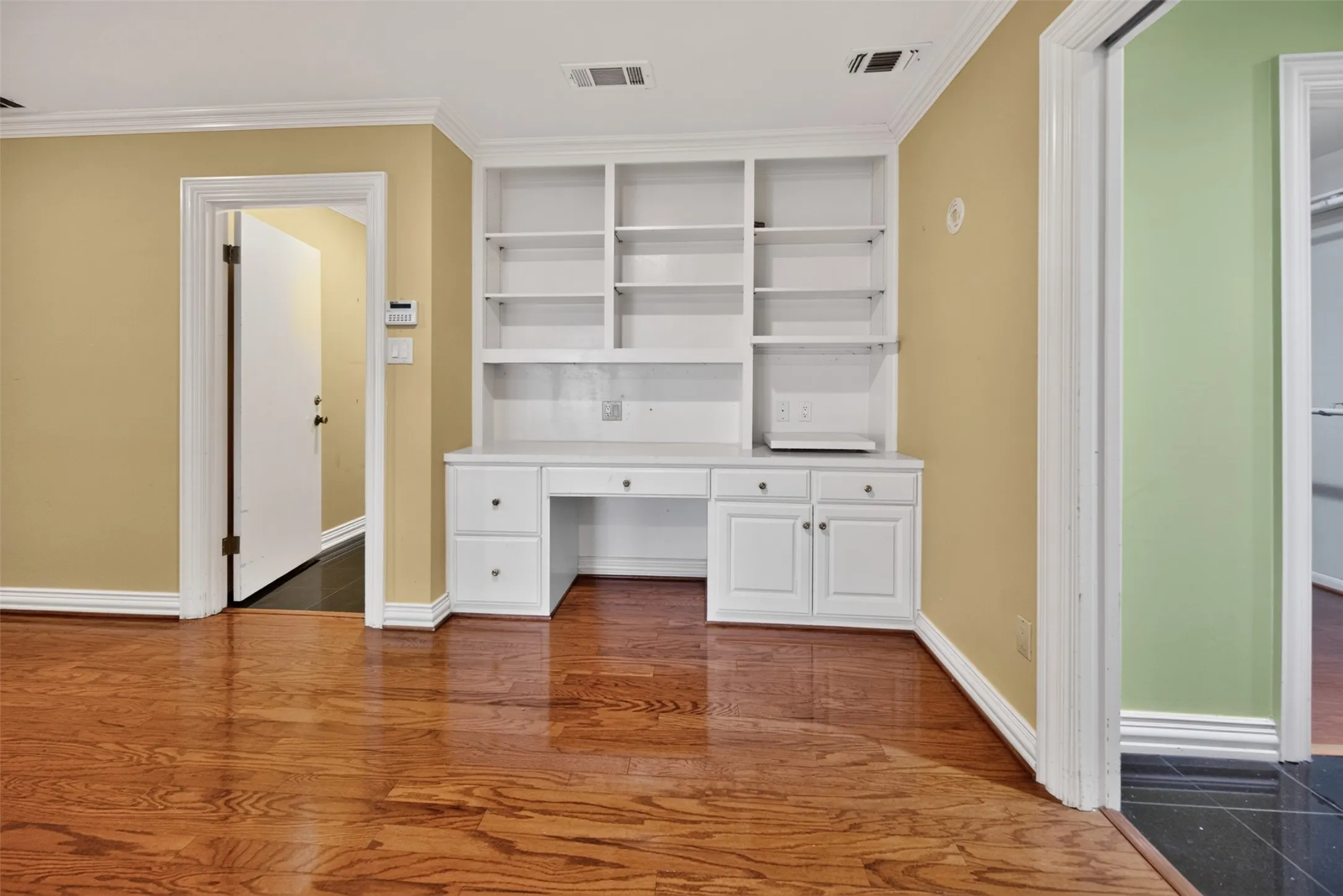 Built-in white cabinetry with desk space and shelving, crown molding, and wood-finish flooring