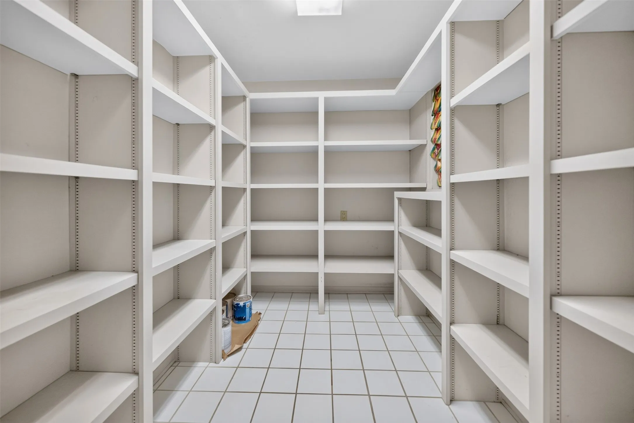 Expansive pantry featuring extensive built-in shelving, white tile flooring, and overhead lighting