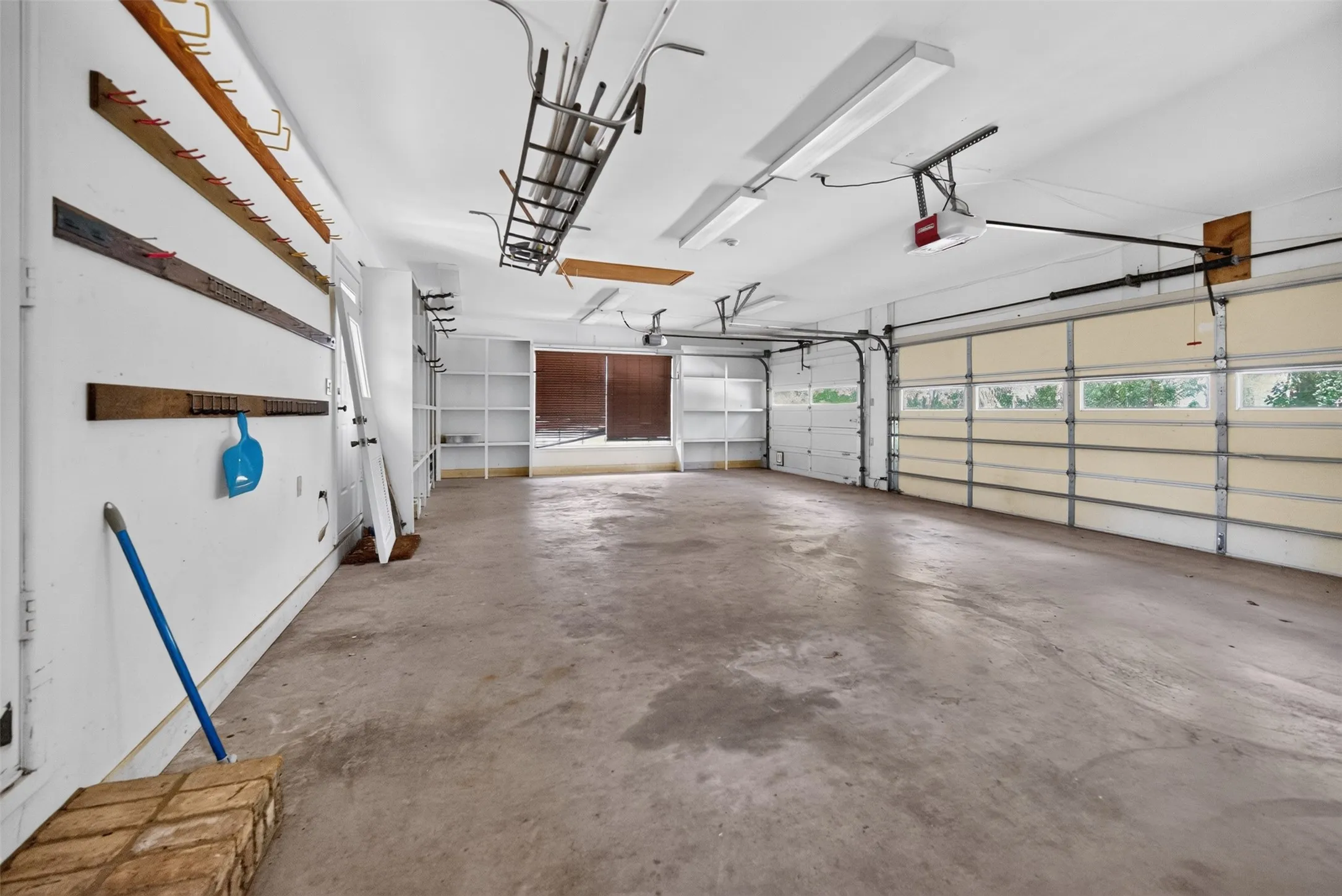 Spacious garage featuring a concrete floor, two overhead doors with window panels, built-in shelving, and bright overhead lighting