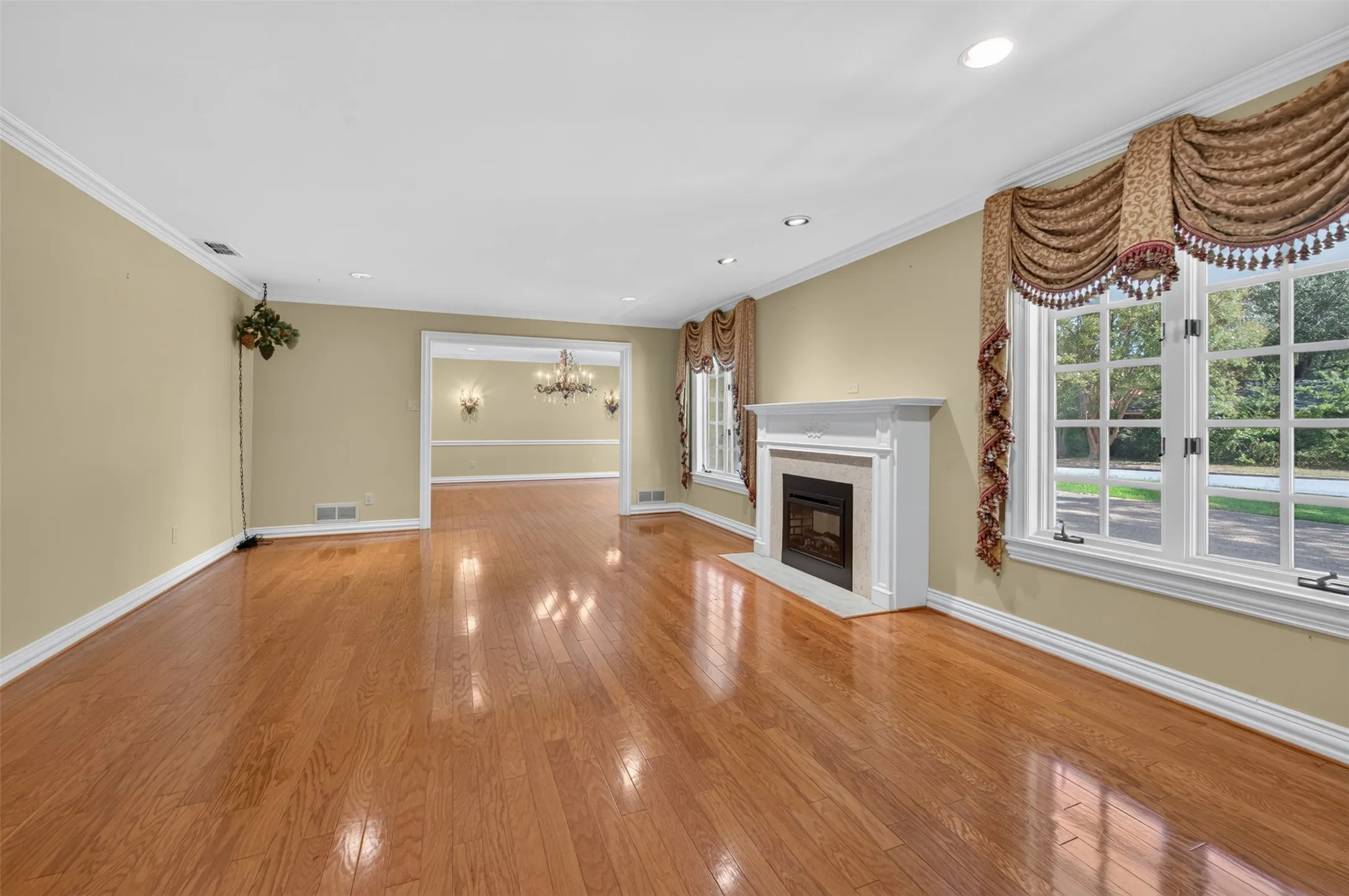 Hardwood flooring, recessed lighting, white mantel fireplace with stone surround, large windows, and crown molding