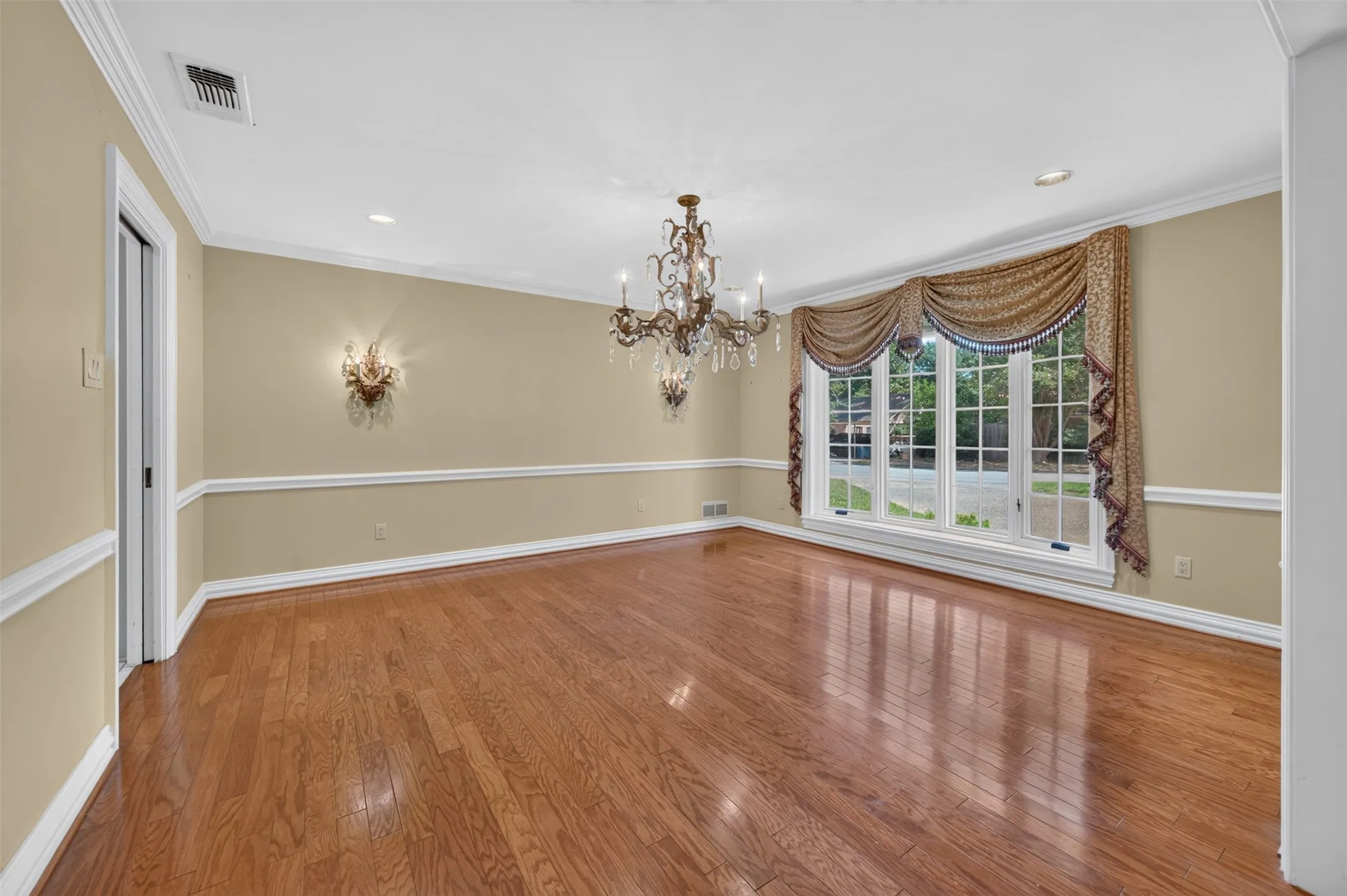 Hardwood flooring, decorative chair rail molding, crown molding, built-in recessed lighting, and a crystal chandelier