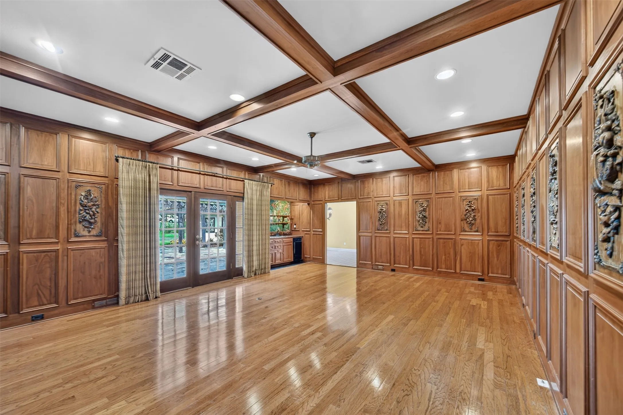 Hardwood flooring throughout, coffered ceiling with recessed lighting, full wood paneling, decorative wall carvings, and French doors