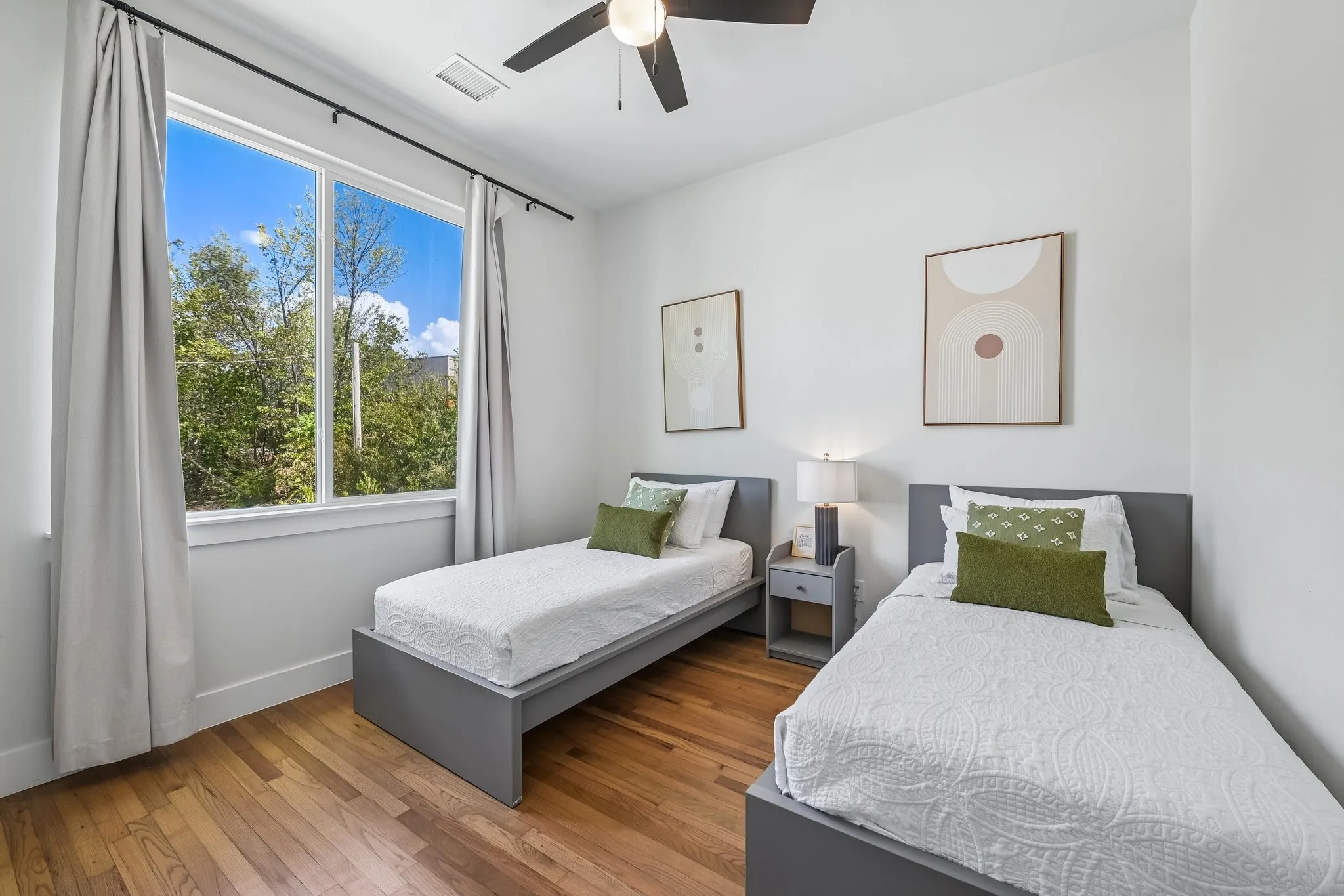 Wood-finish flooring with white baseboards, large window with white framing, and a ceiling fan with integrated lighting