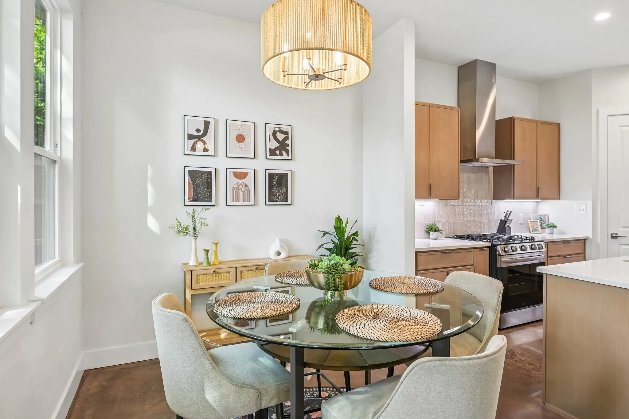 Open-concept layout featuring a kitchen with wood-finish cabinetry, stainless steel range, and range hood, complemented by a dining area with a glass-top table and an overhead woven chandelier