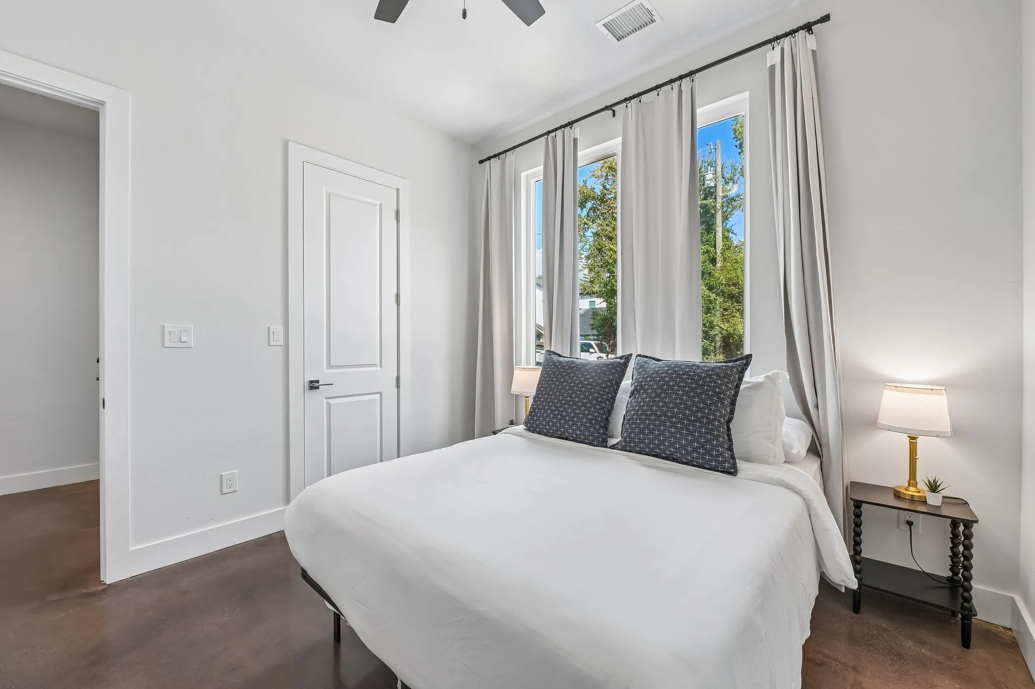Three tall windows with privacy curtains, a ceiling fan, and a paneled door with dark hardware