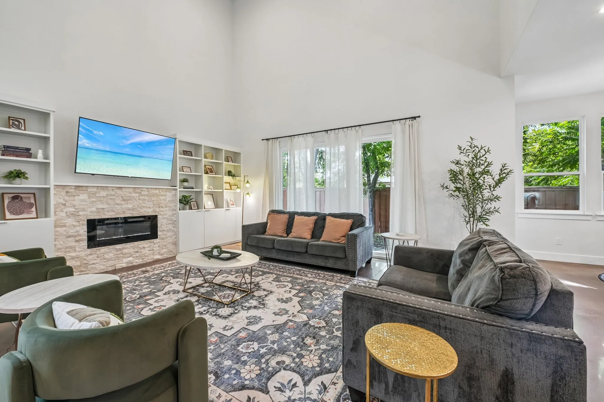 Vaulted ceiling living area featuring a stone-faced electric fireplace, built-in shelving, and large windows