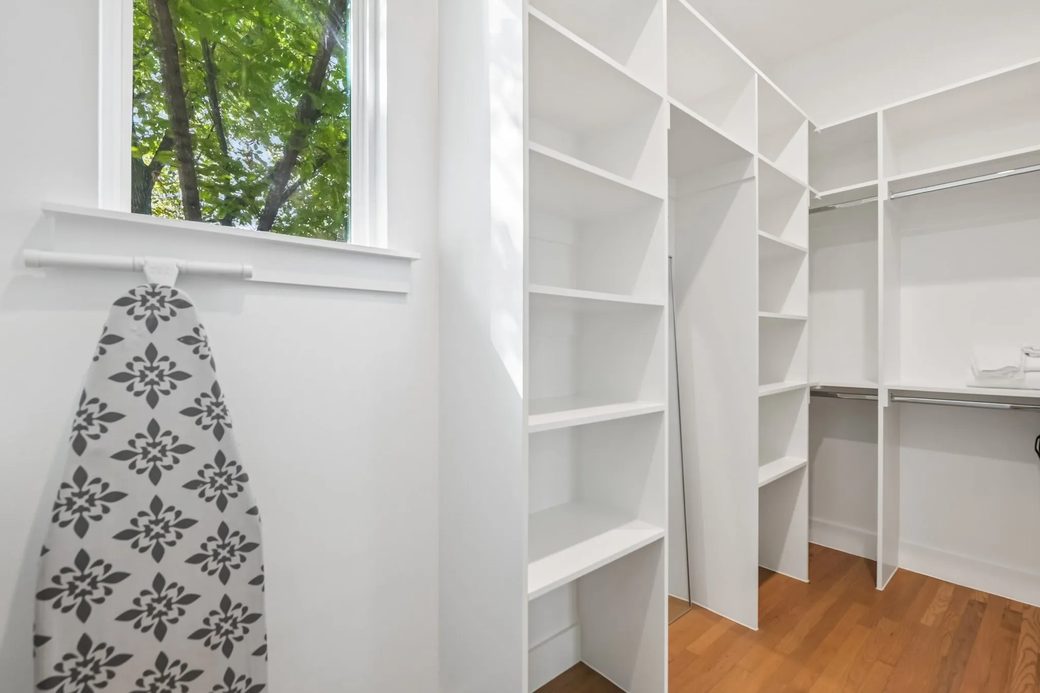 Custom closet system featuring multiple shelves and hanging rods, durable wood flooring, and a window with white trim