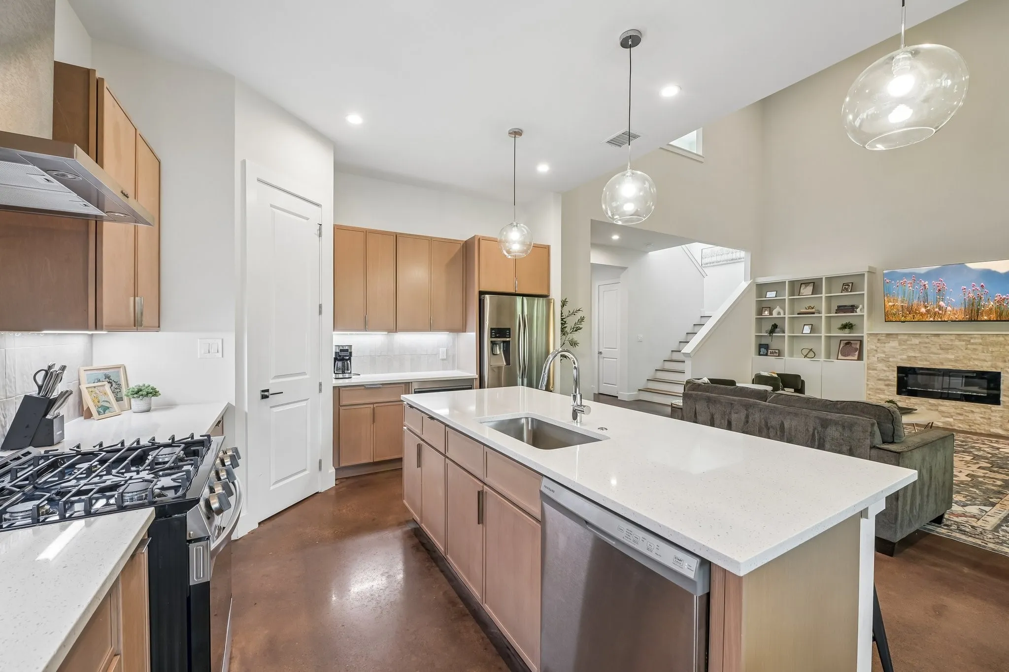 Kitchen island with integrated sink, stainless steel appliances, light wood-finish cabinetry, and white countertops
