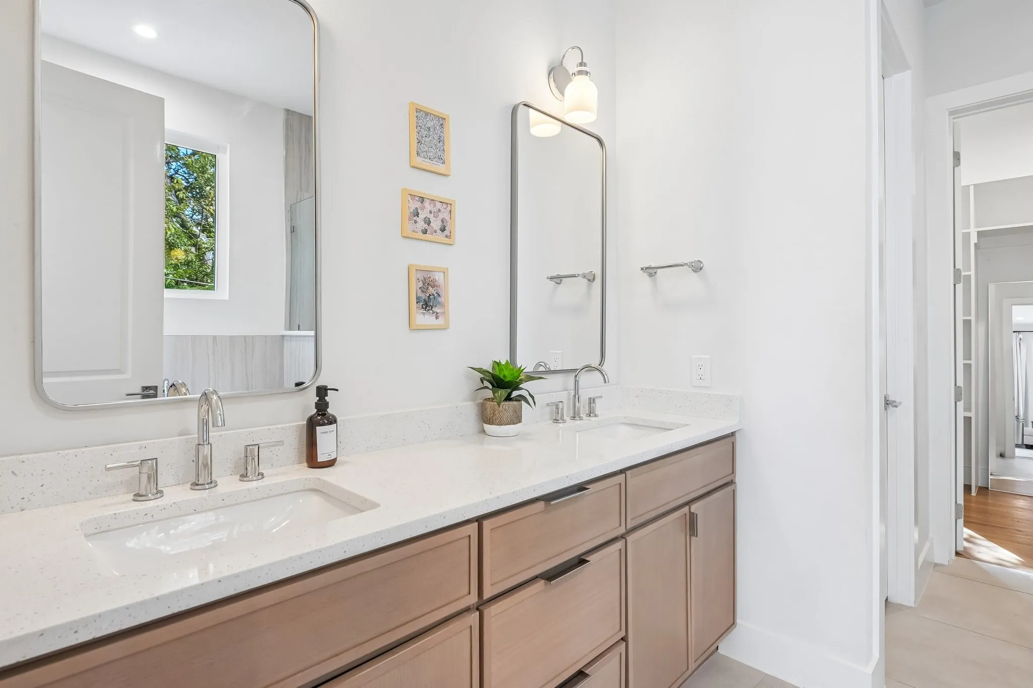 Dual under-mount sinks with polished chrome fixtures, light-toned wood-finish cabinetry, and framed mirrors