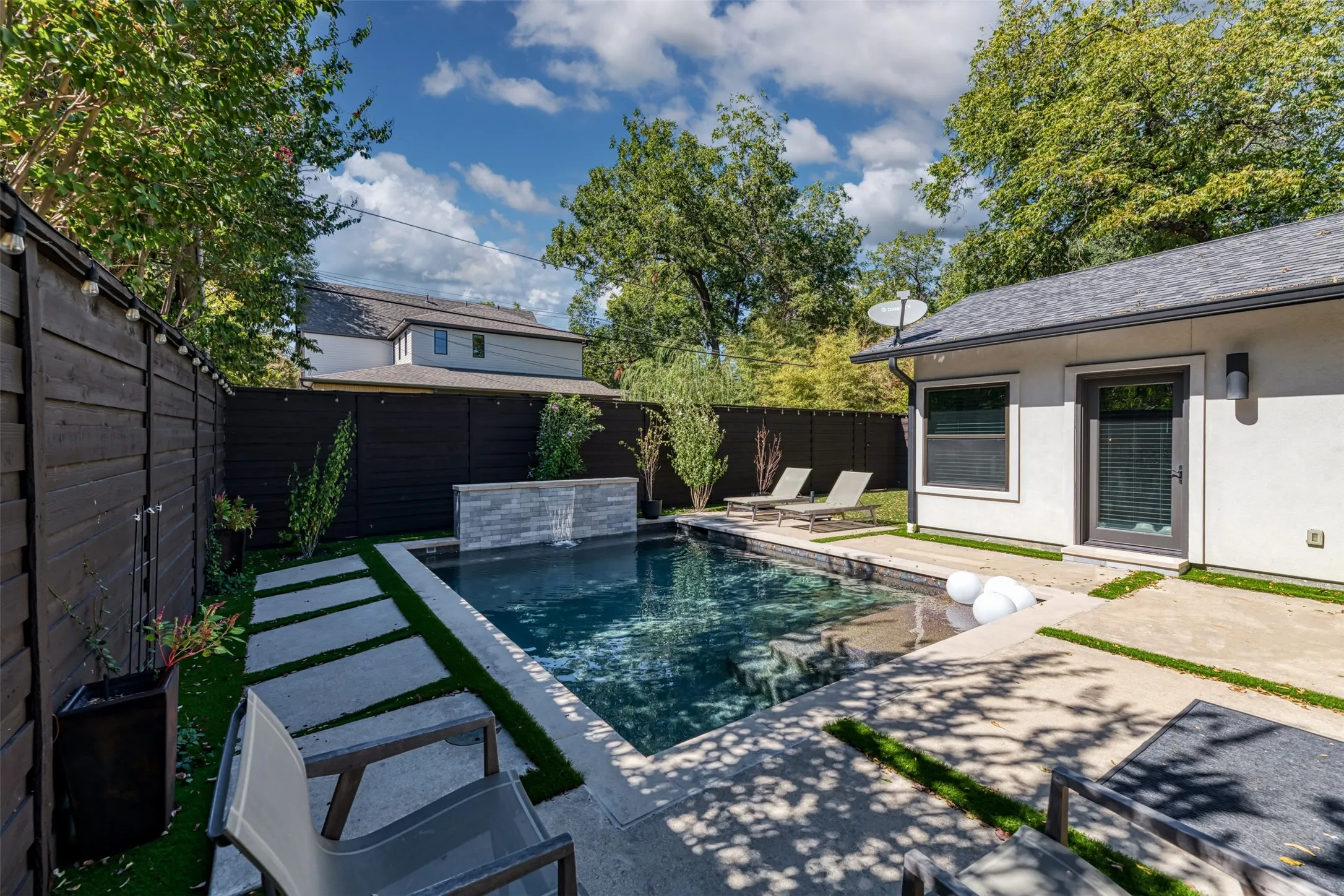 Outdoor pool with a stone water feature, framed by a dark wood-finish privacy fence