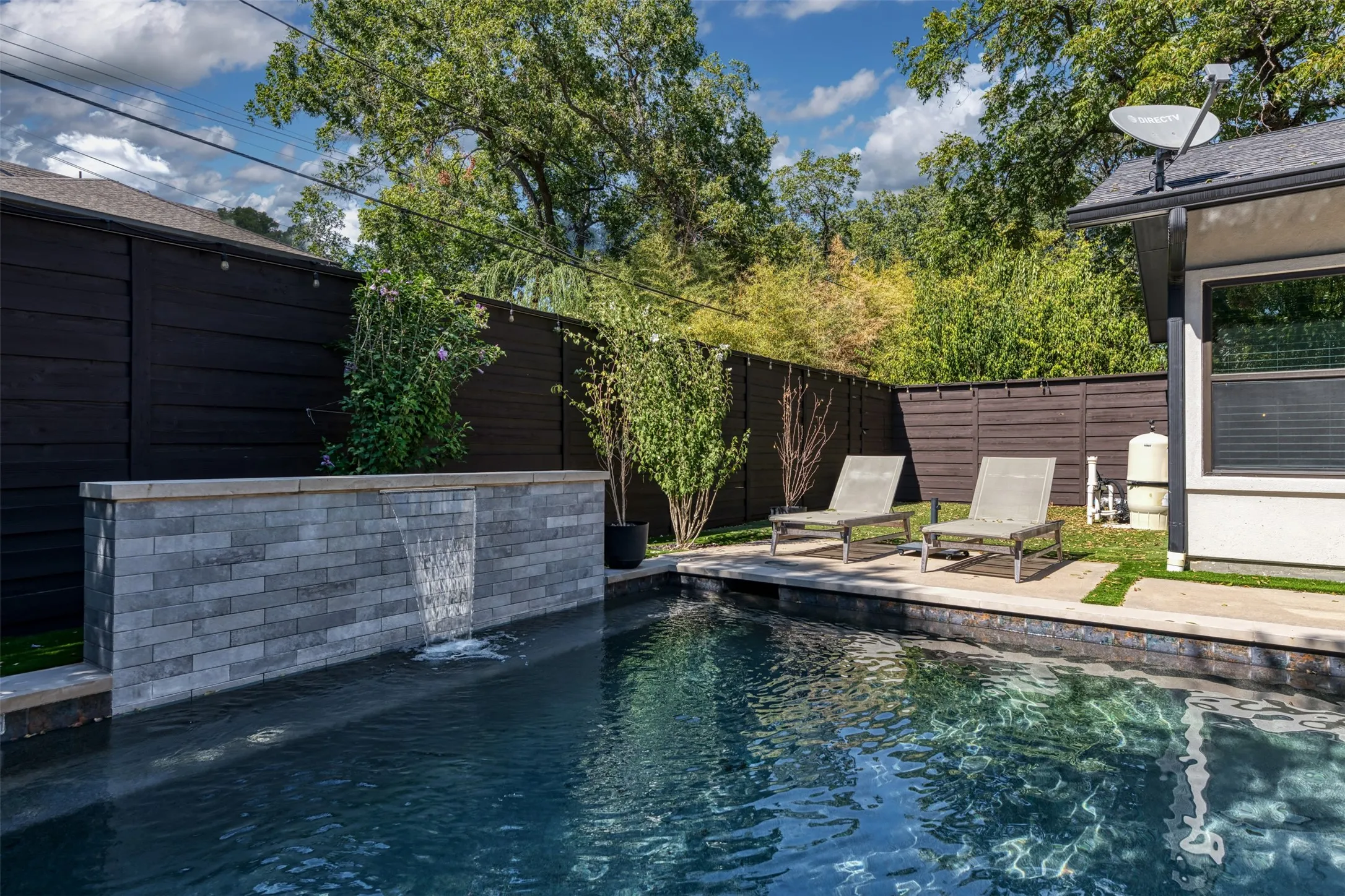Private backyard featuring a swimming pool with a stone water feature, perimeter fencing, and concrete patio areas