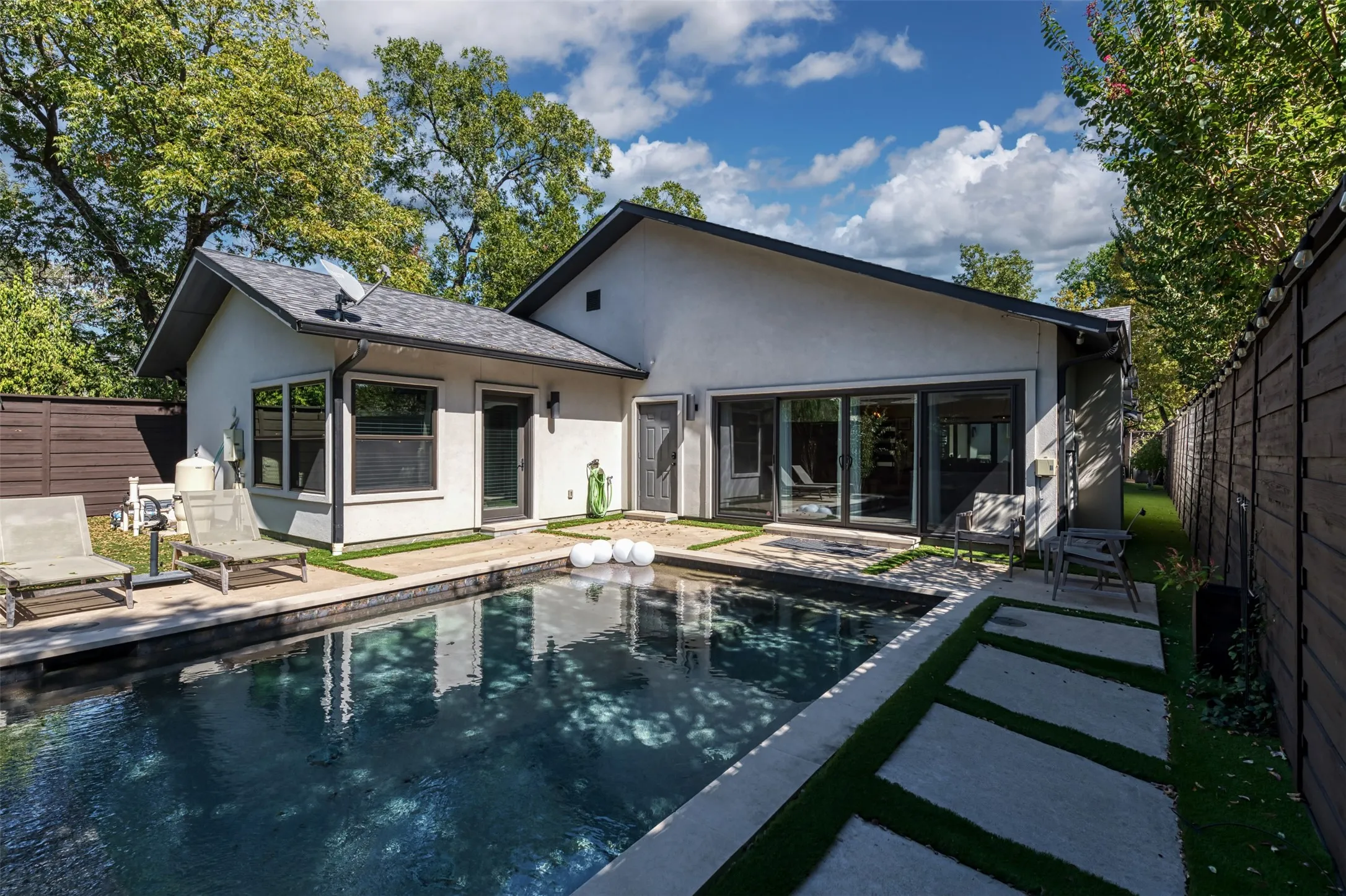 Exterior stucco siding with a dark-tiled roof, featuring a built-in swimming pool with surrounding hardscaping, and a privacy fence
