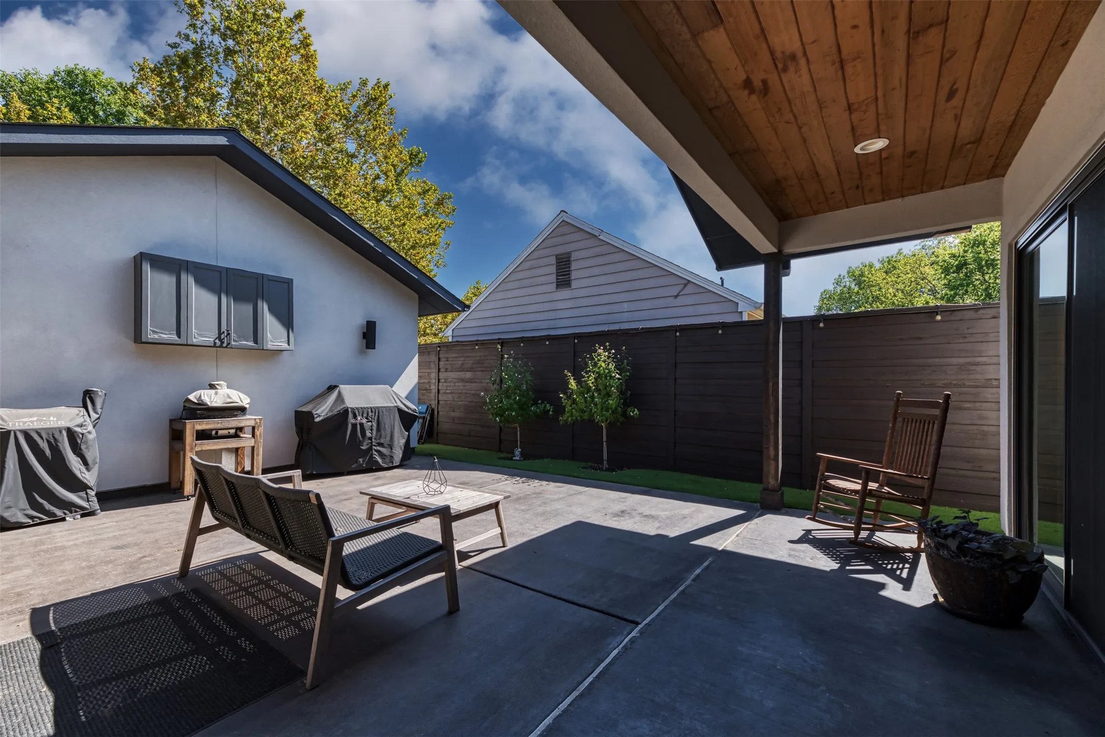 Covered patio with a wood-plank ceiling, concrete flooring, sliding glass door, built-in outdoor cabinetry, and a dark wood privacy fence