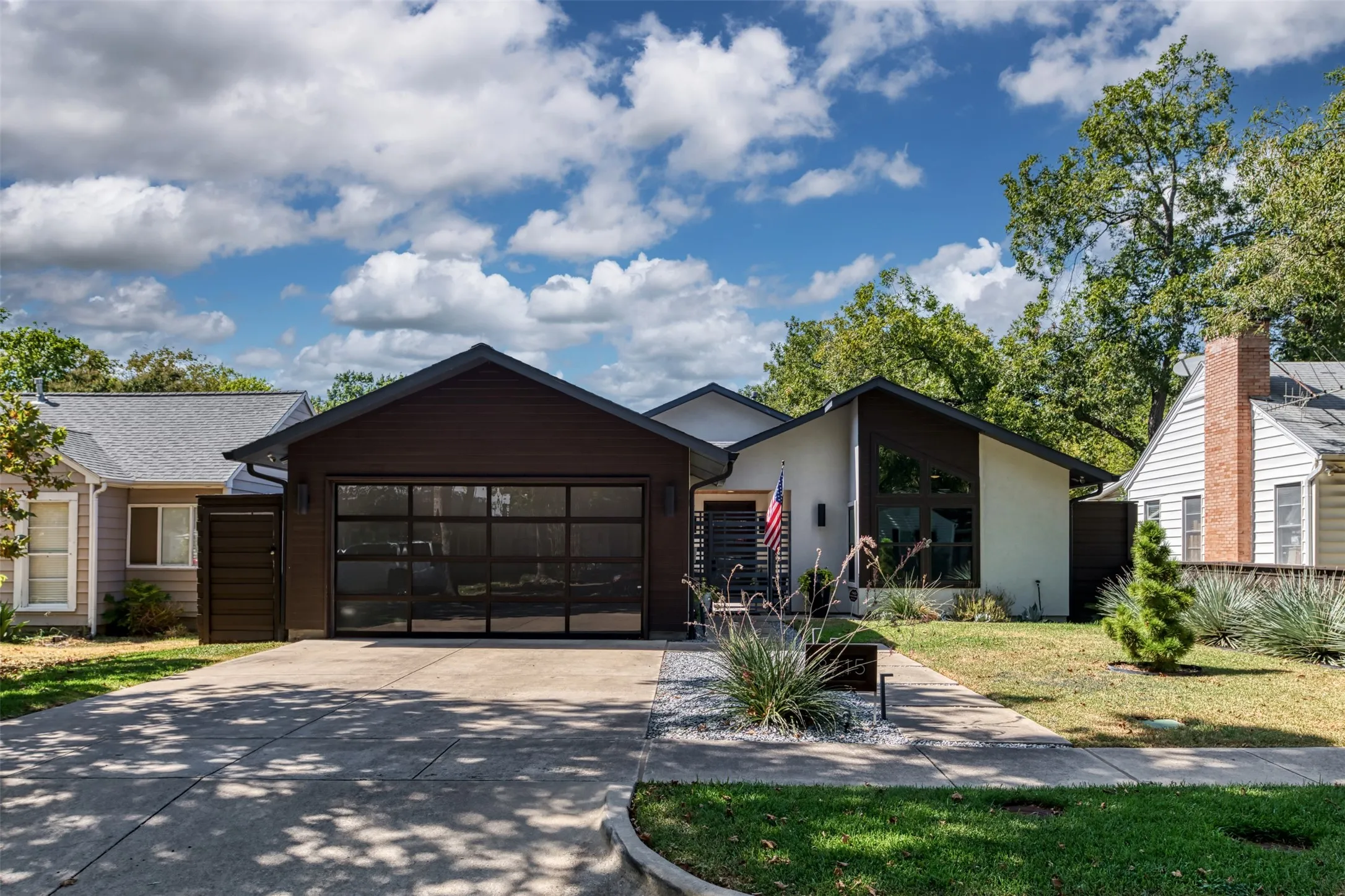 Contemporary exterior with a glass-paneled garage door, a concrete driveway, and a landscaped front yard featuring white gravel and greenery