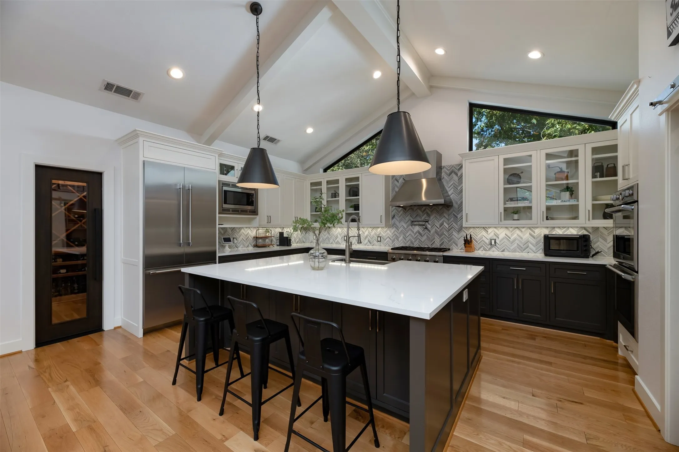 Vaulted ceiling kitchen featuring a large central island with a solid surface countertop, stainless steel appliances, herringbone tile backsplash, and light wood-finish flooring