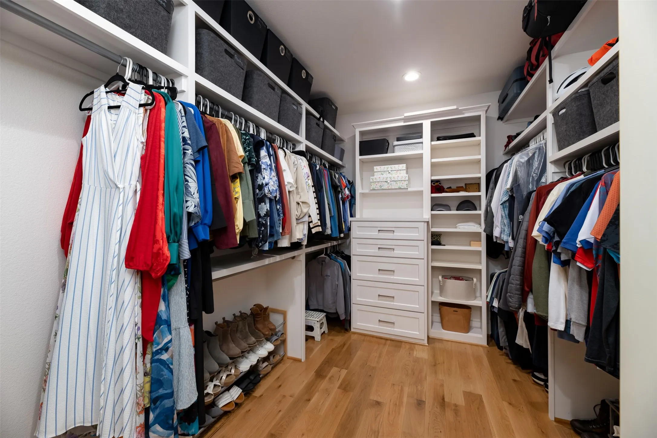 Custom built-in white cabinetry with chrome hardware, extensive hanging rods, multiple open shelves, recessed lighting, and wood-finish flooring