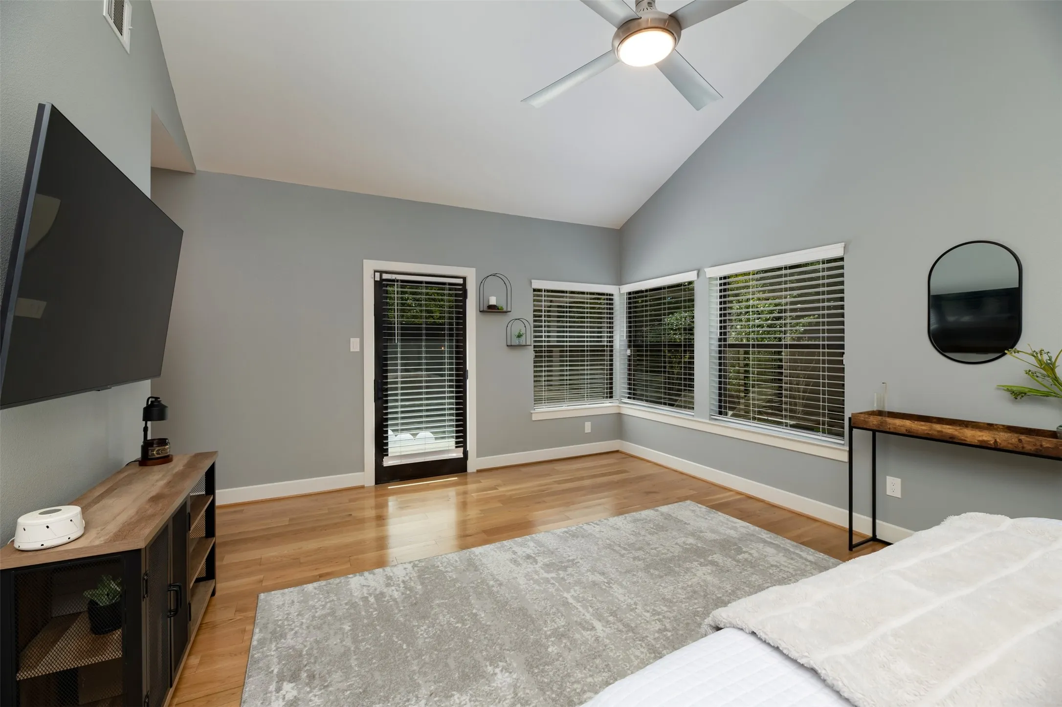 Vaulted ceiling with a ceiling fan, light wood-finish flooring, and multiple windows with blinds