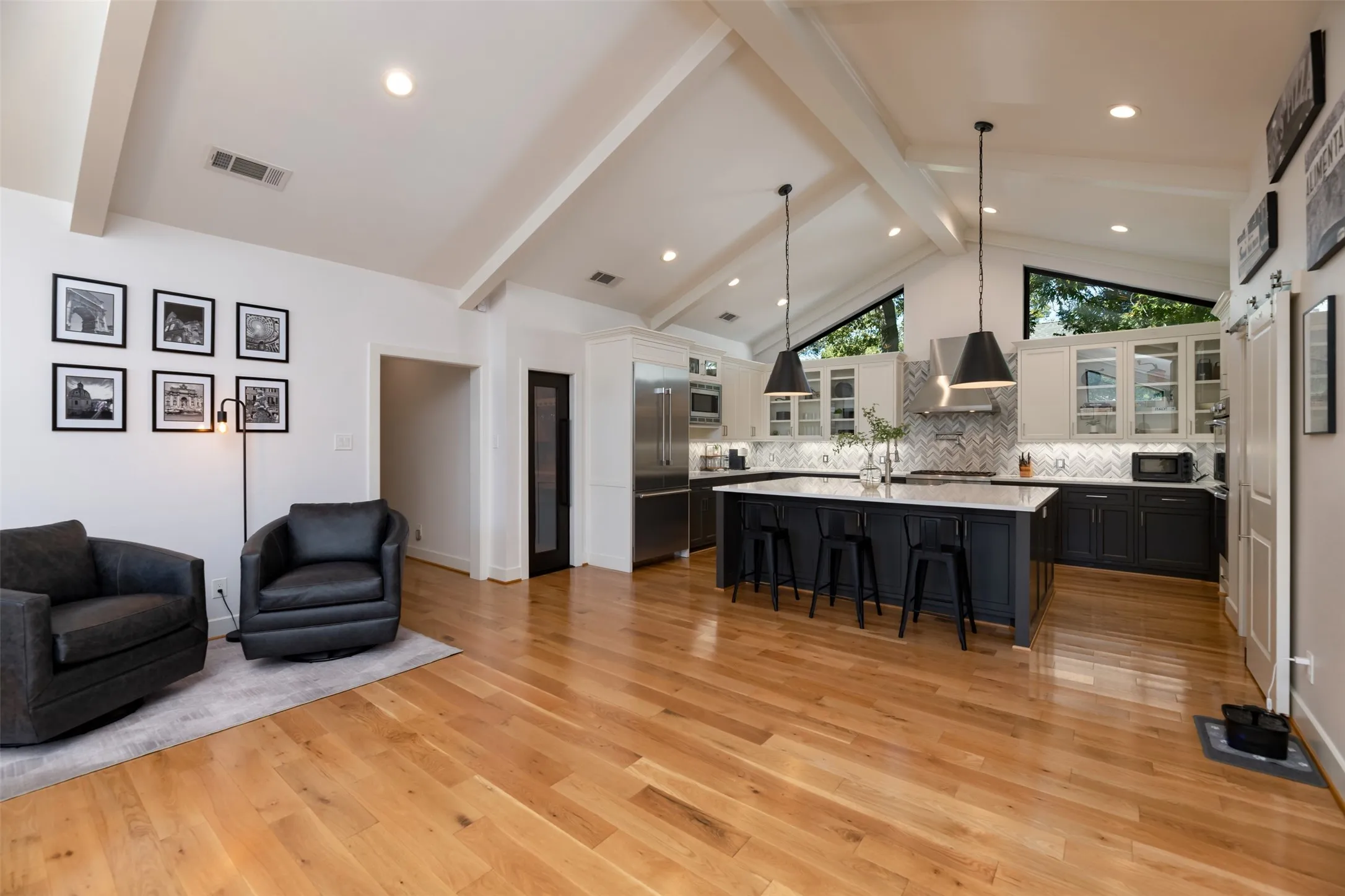 Vaulted ceiling with exposed beams, recessed lighting, wood-finish flooring, two-tone kitchen cabinetry, and a large center island with pendant lighting
