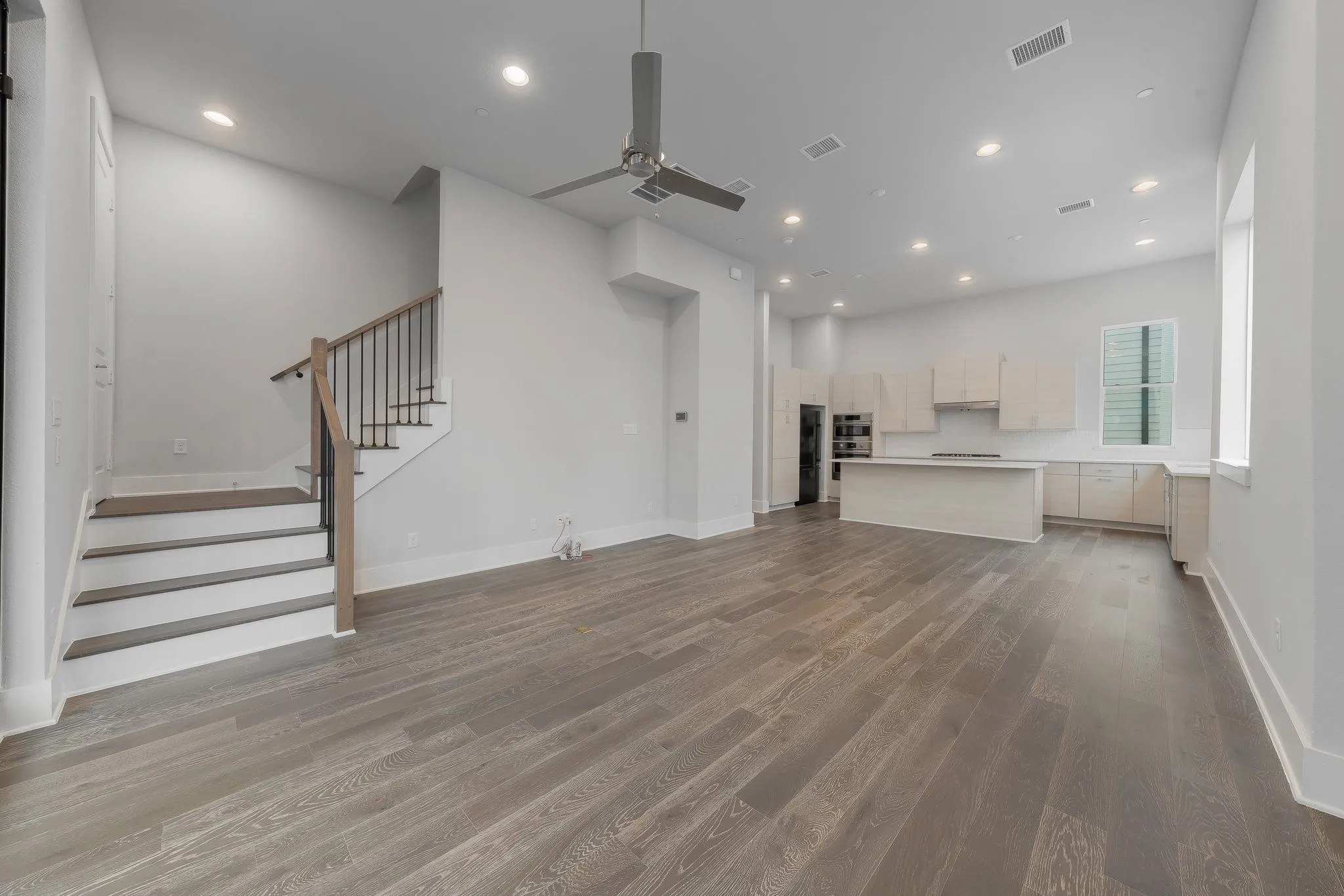 Unfurnished living room with stairs, a ceiling fan, wood finished floors, and visible vents