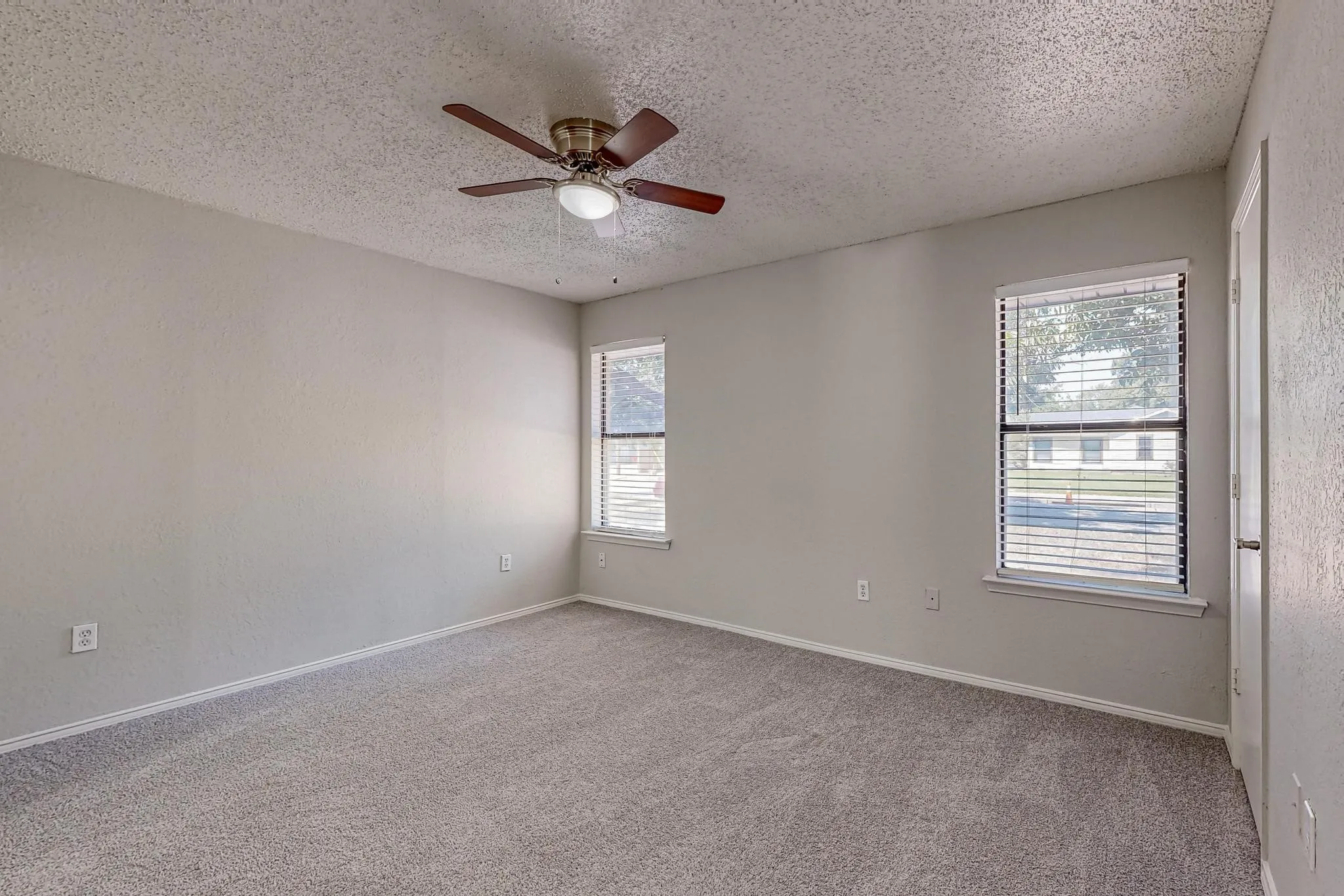 Neutral wall tones, ceiling fan with light fixture, two windows with blinds, and soft carpeting