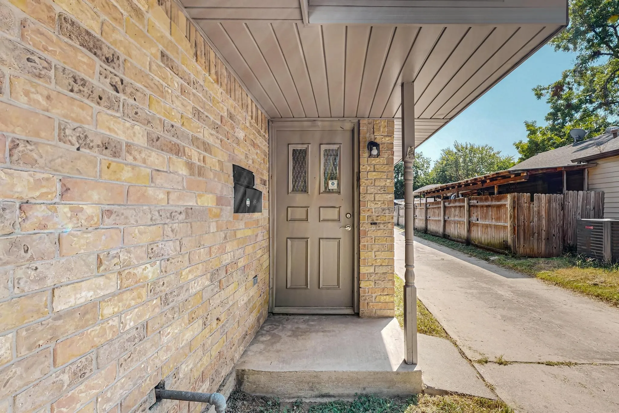 Brick exterior with a covered entry, concrete walkway, and a privacy fence