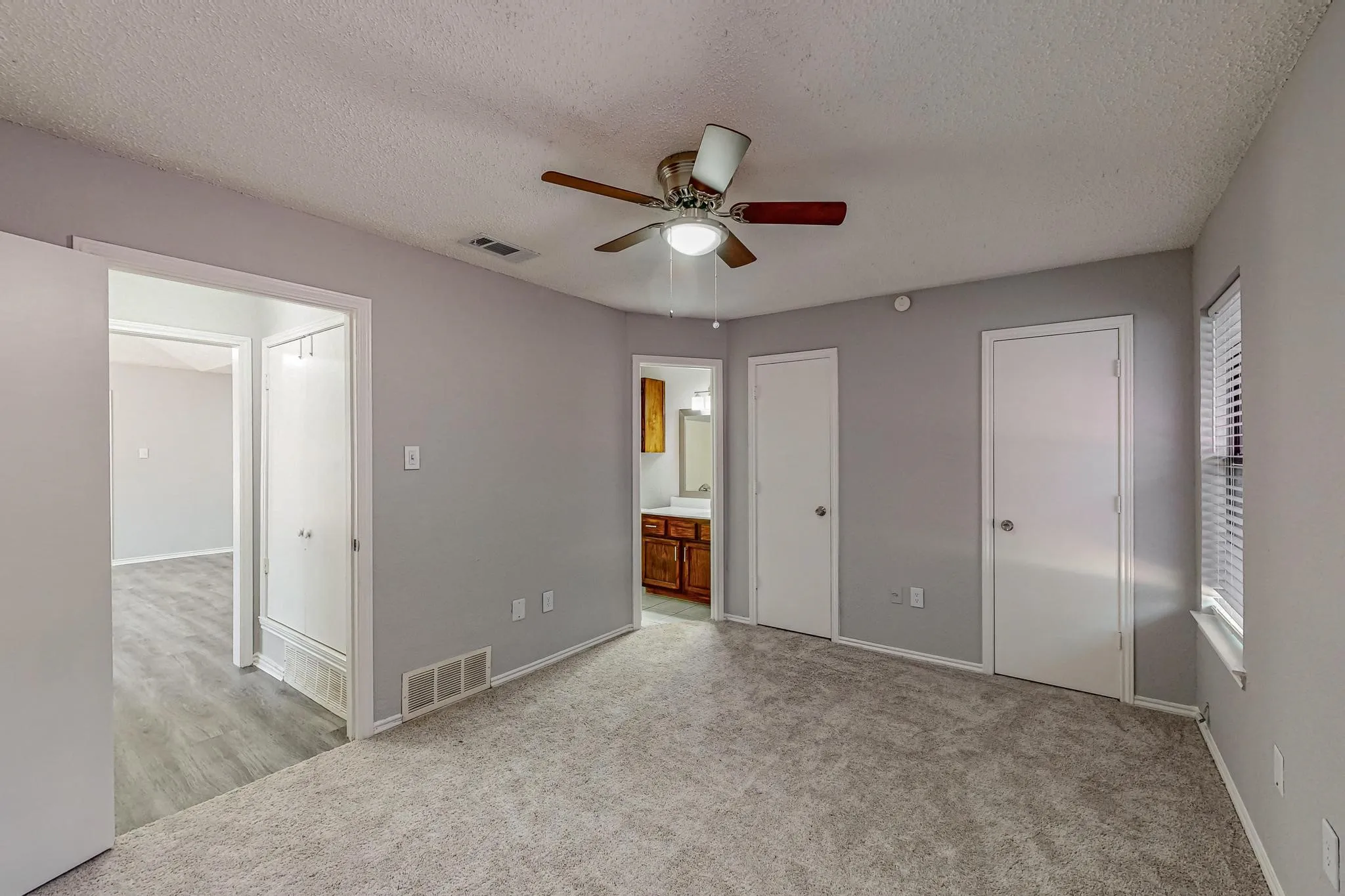 Carpeted room with a ceiling fan, white doors, and a window with blinds