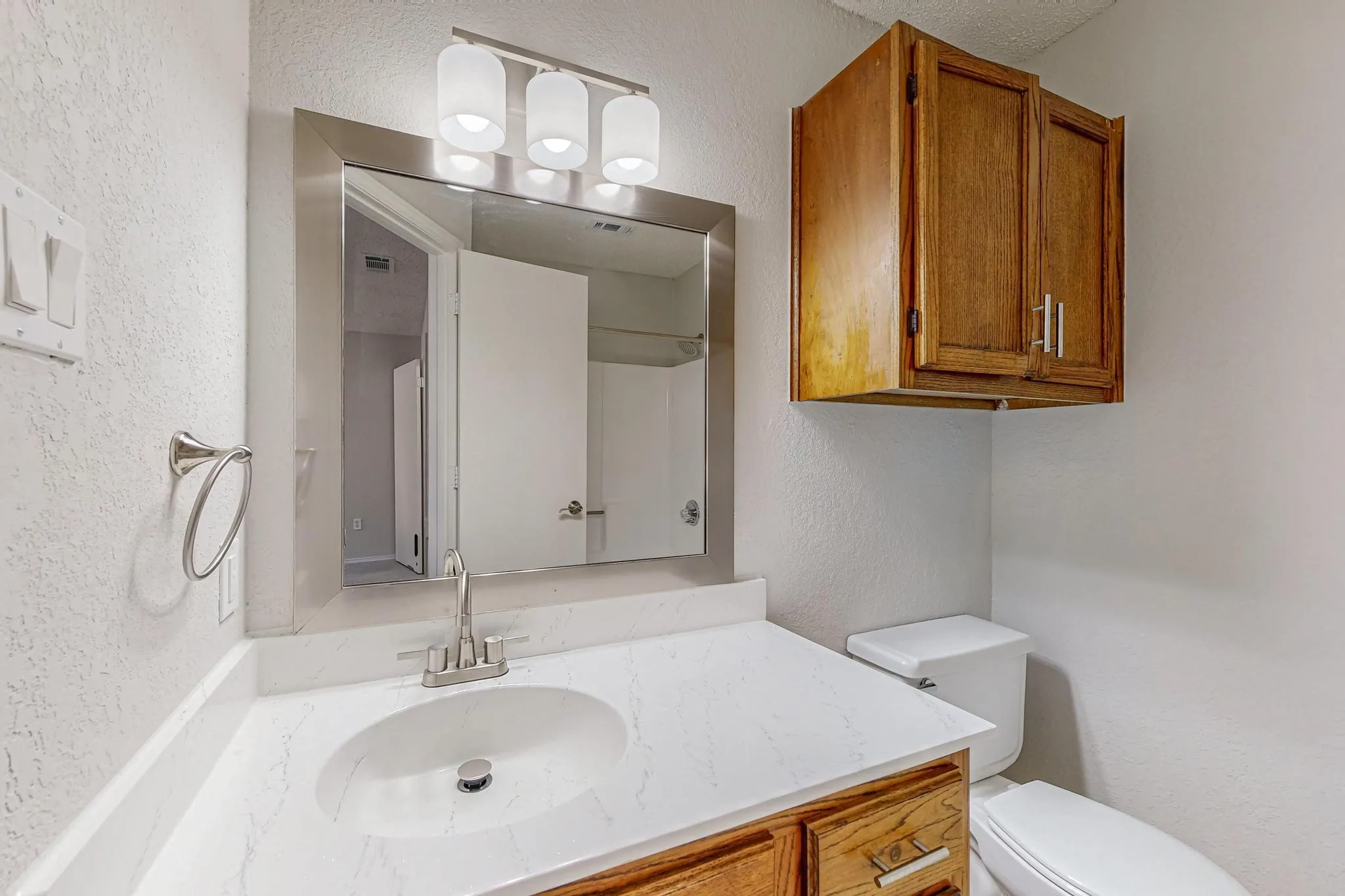 Vanity with white countertop and integrated sink, brushed nickel faucet, wall-mounted mirror, and overhead tri-bulb light fixture