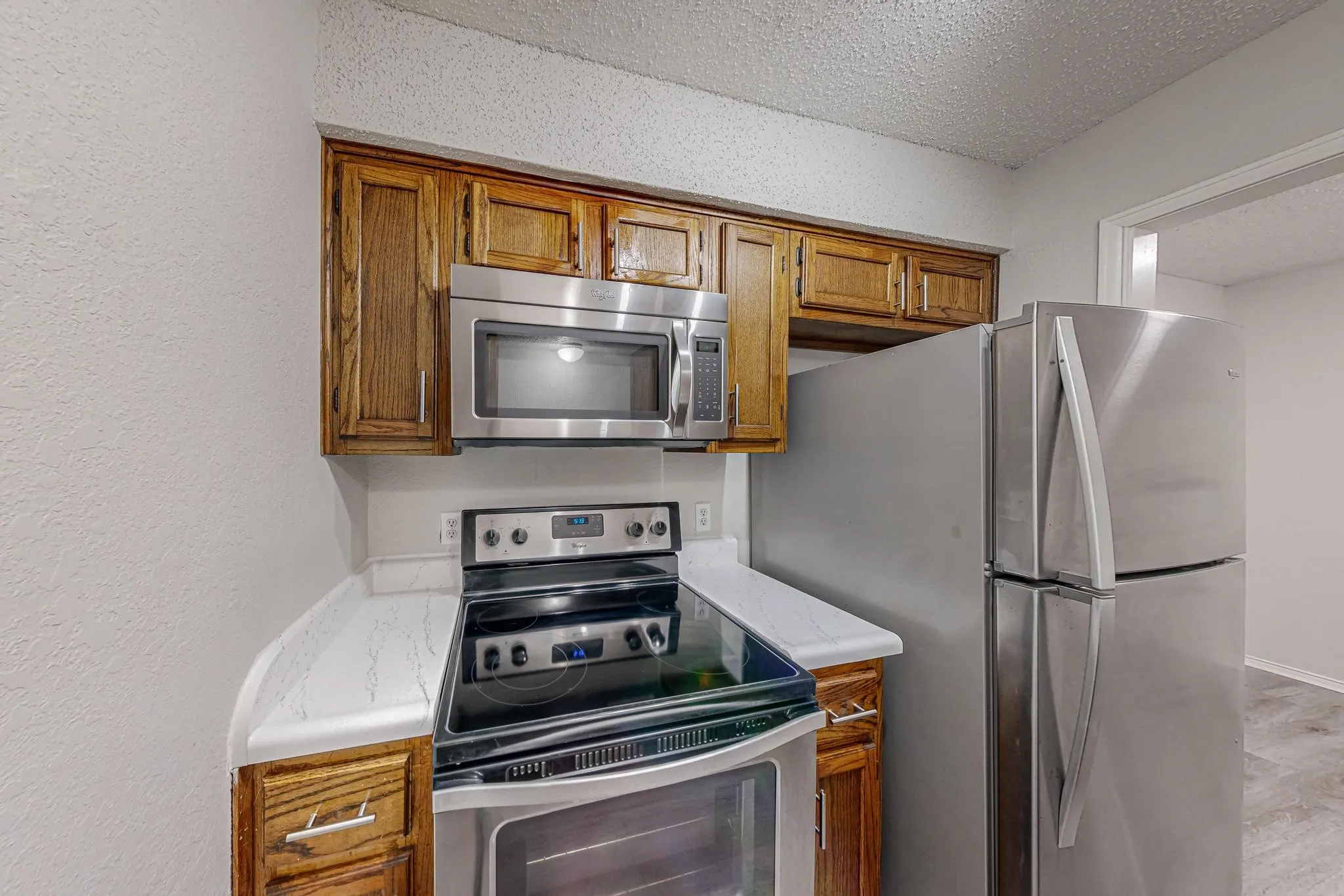 Stainless steel appliance suite, wood cabinetry, solid surface countertops, and an electric range with an overhead microwave