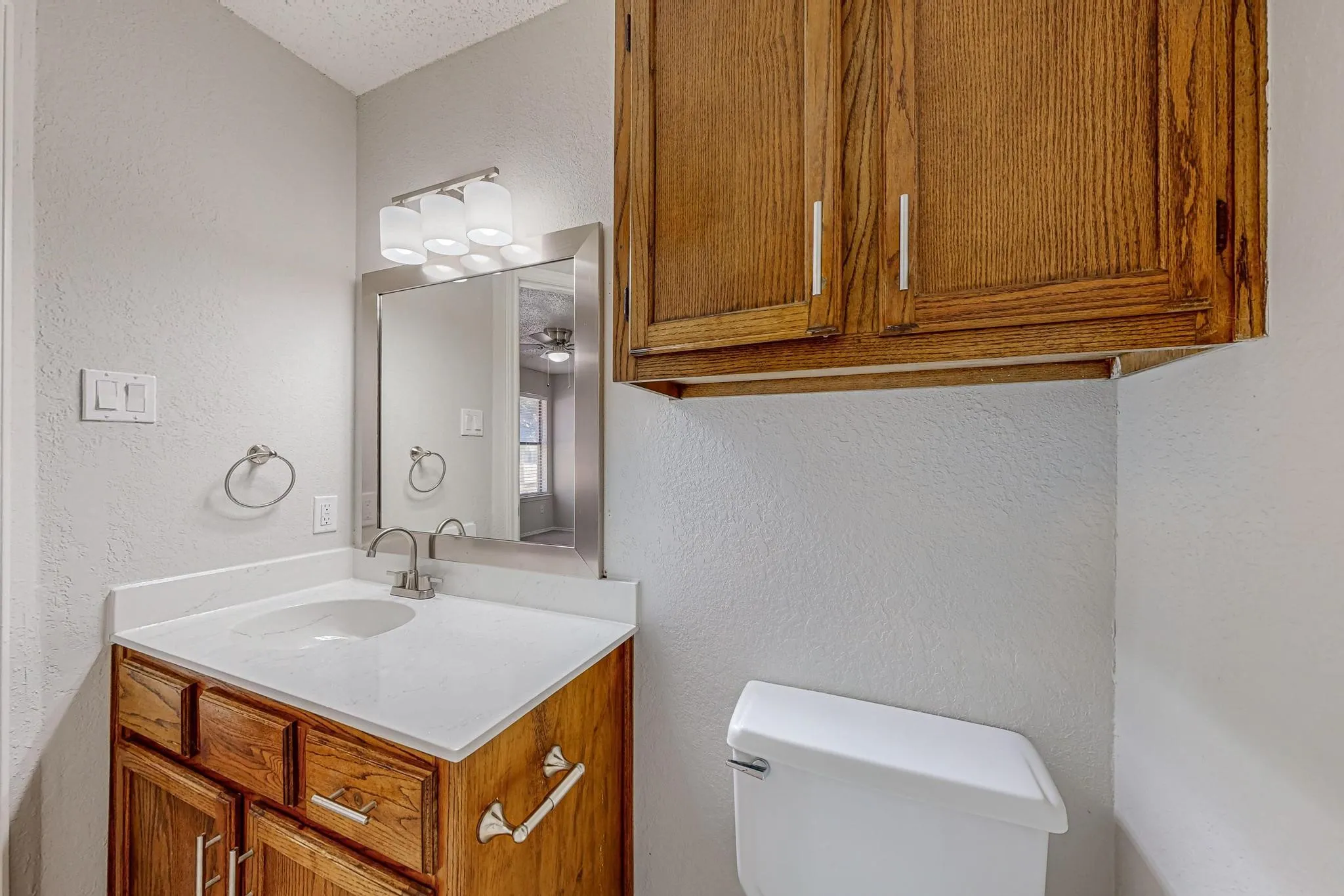 Wood-finish vanity with white countertop, undermount sink, and chrome faucet