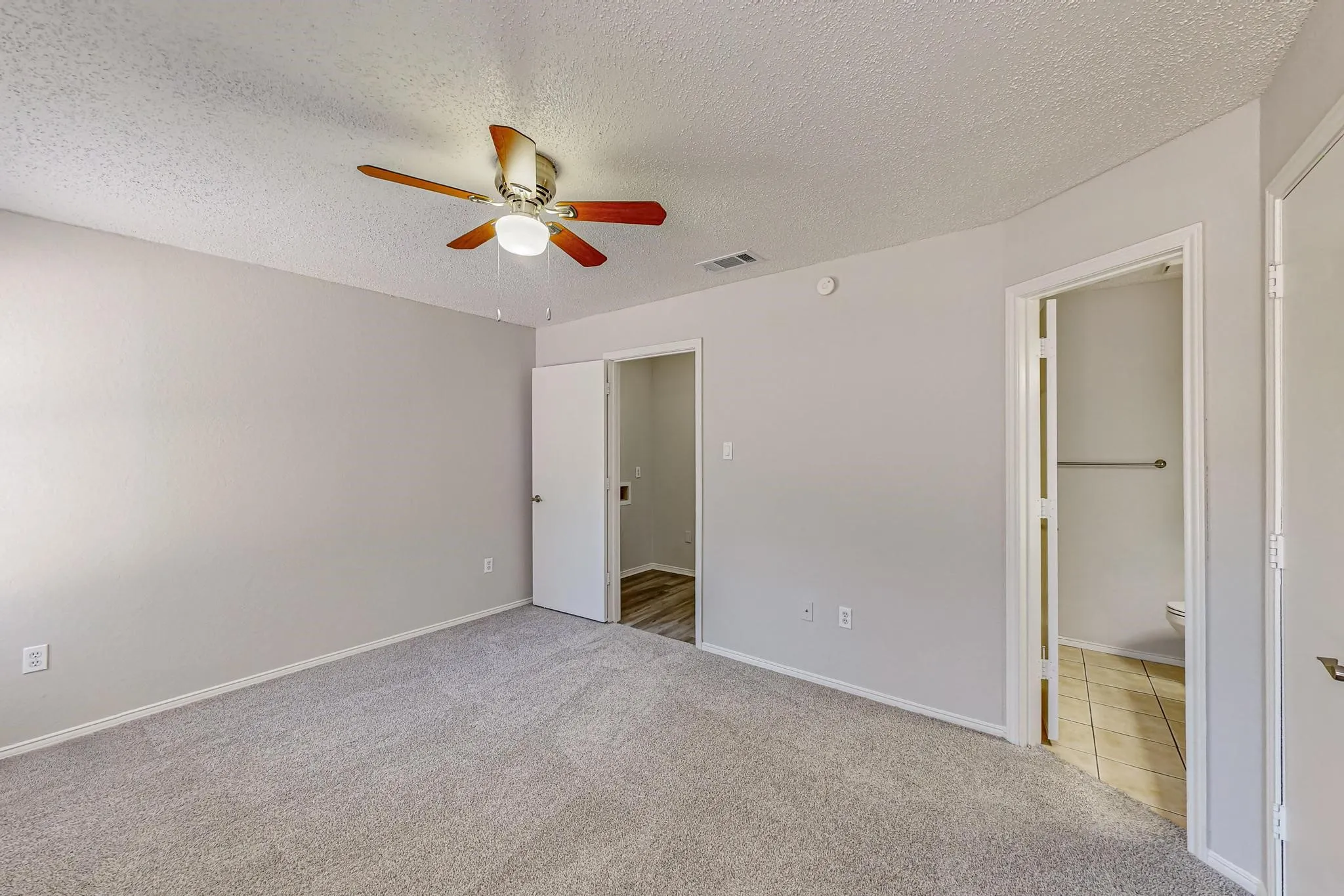 Plush carpeting, light grey wall paint, ceiling fan with wood-finish blades, white trim, and a tile-floor bathroom