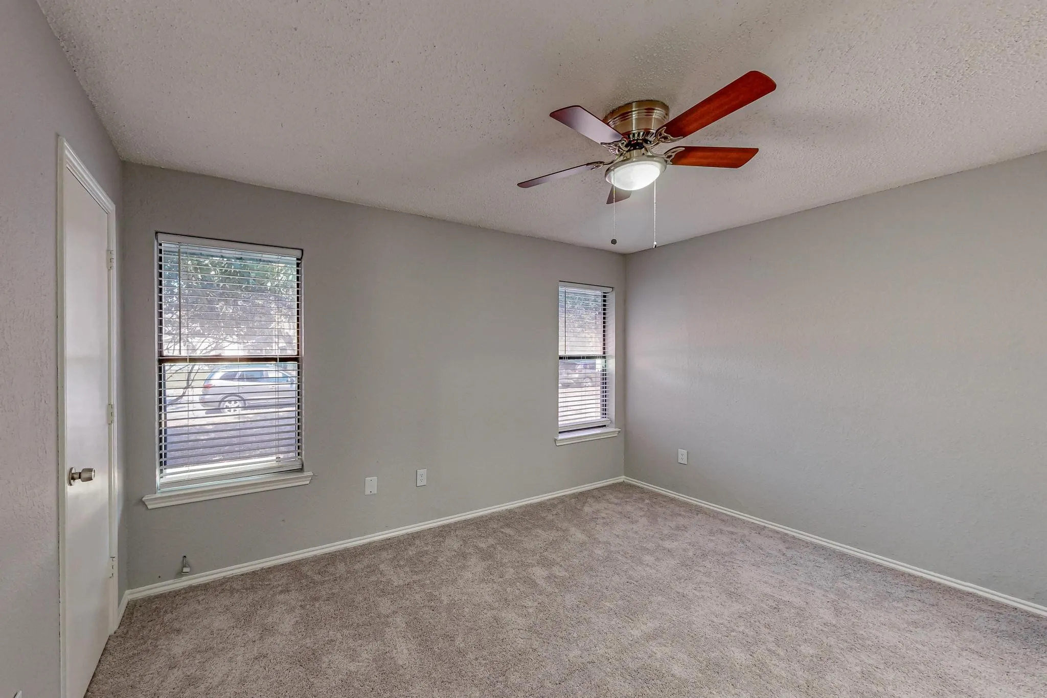 Neutral paint tones, two windows with blinds, ceiling fan with integrated lighting, and carpet flooring