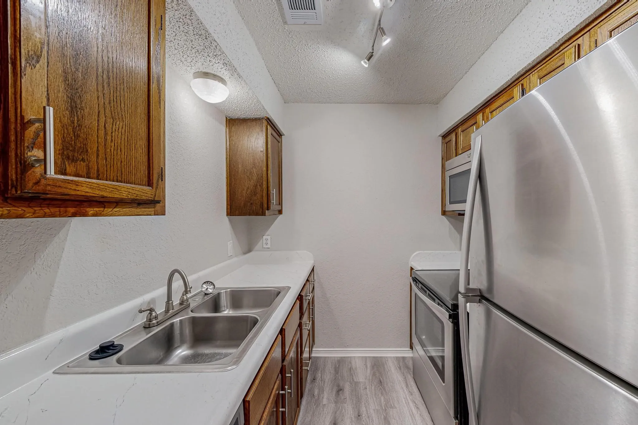 Kitchen with wood-finish cabinetry, white countertops, a double basin stainless steel sink, wood-finish flooring, and stainless steel appliances