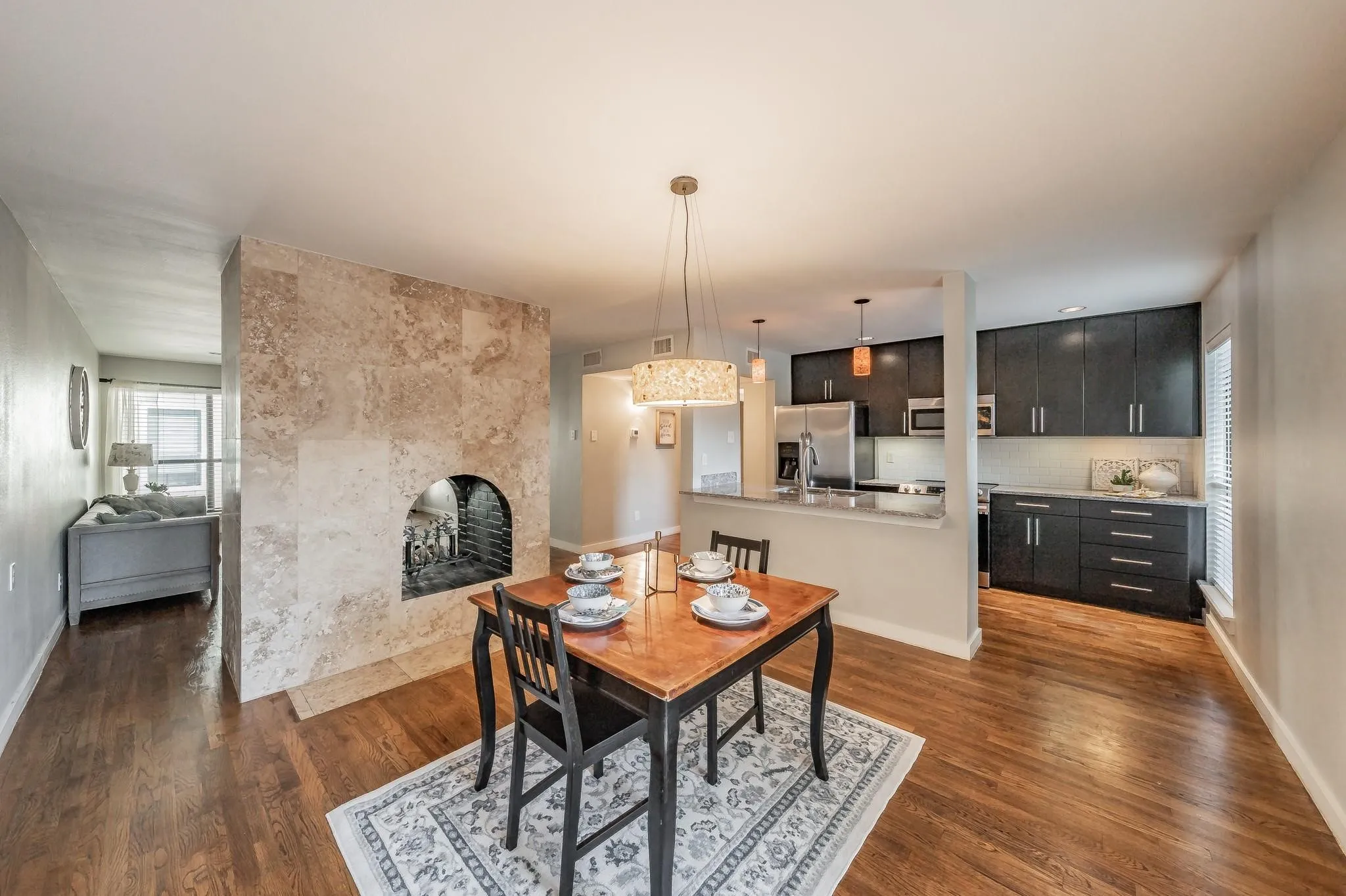 Stone-clad fireplace with hearth, wood-finish flooring, dark cabinetry, stainless steel appliances, and a kitchen peninsula