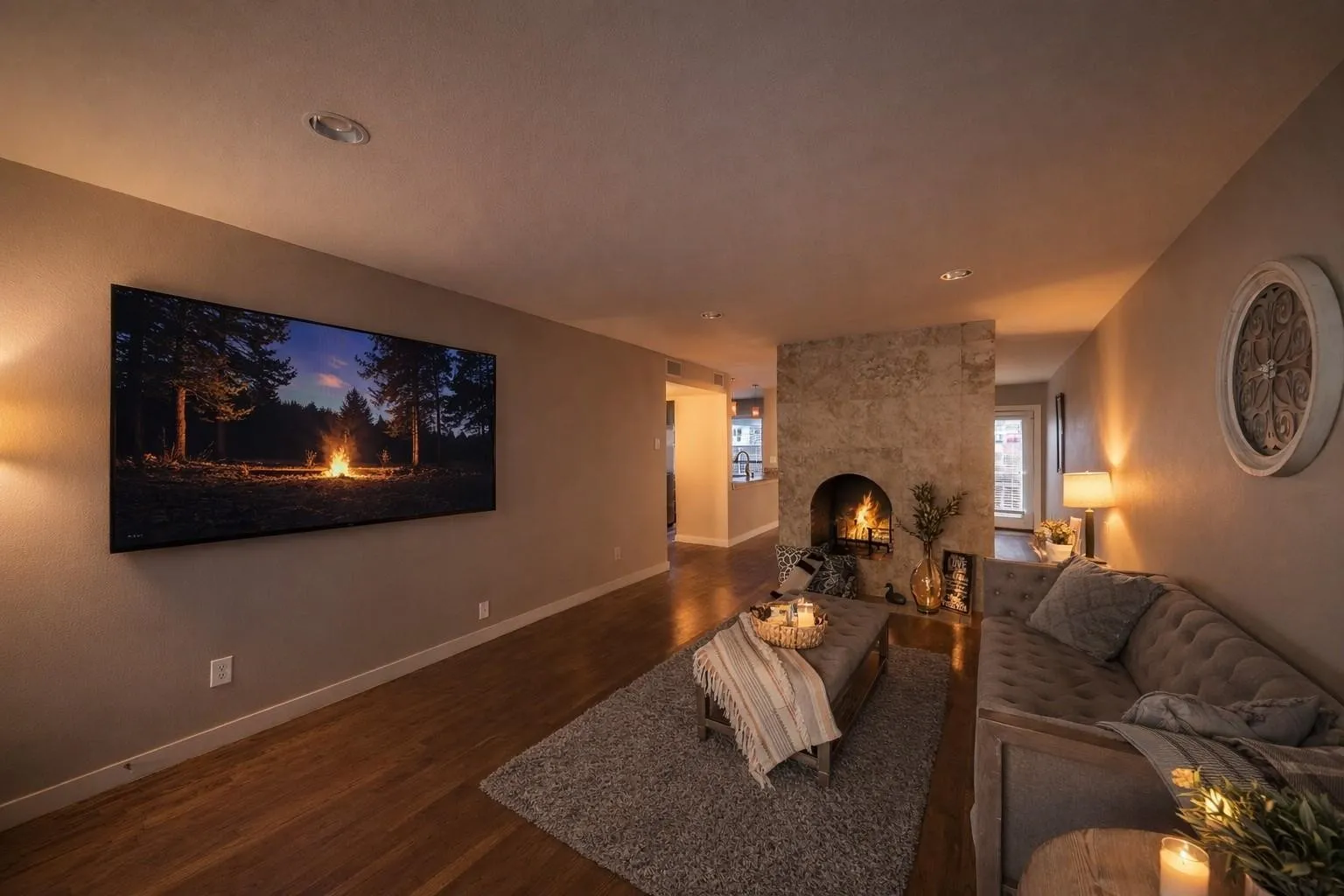 Stone-clad fireplace with arch opening, recessed ceiling lighting, wood-finish flooring, and a flat wall-mounted display