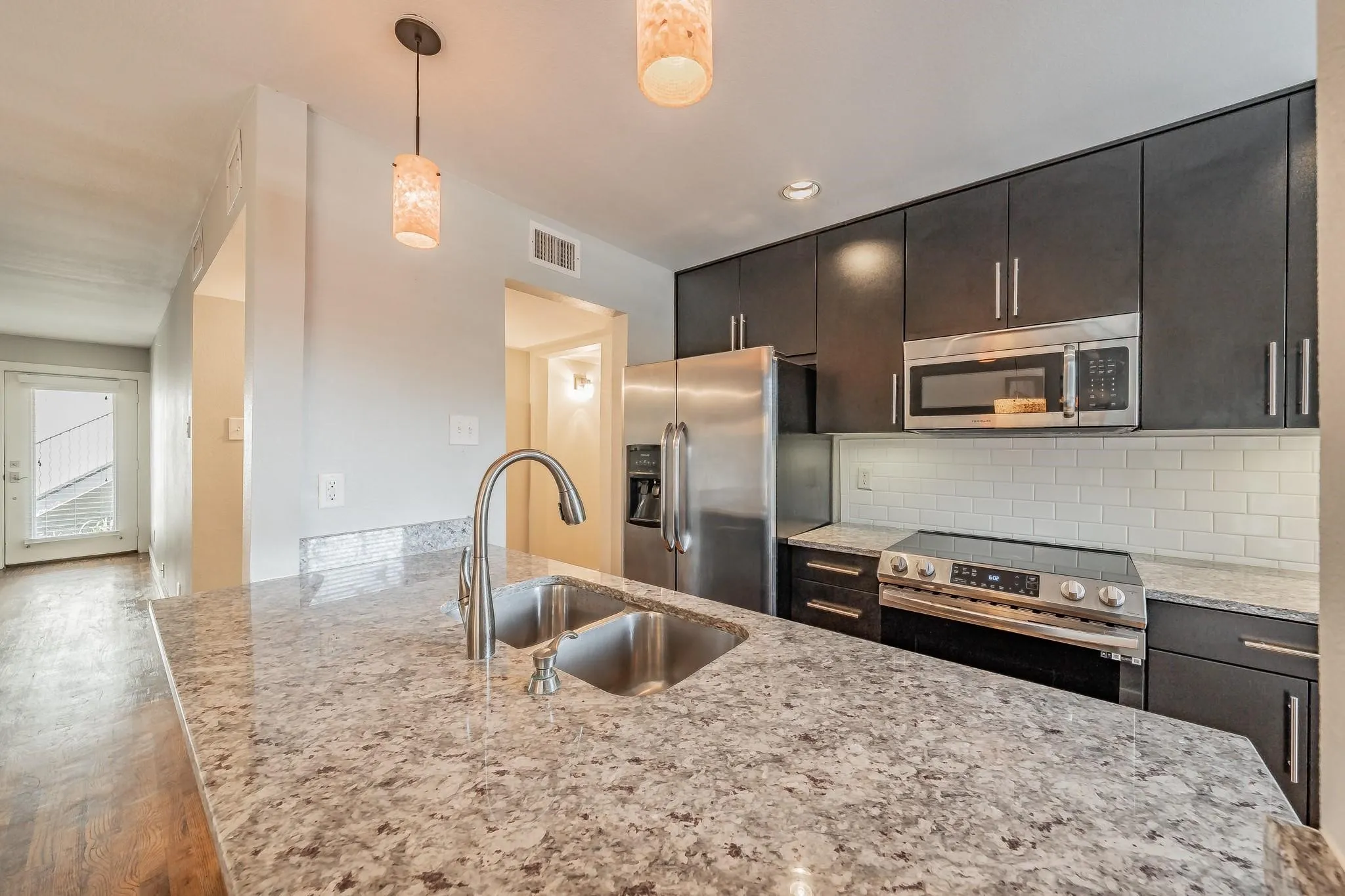 Kitchen featuring stainless steel appliances, dark wood-finish cabinetry, light-toned countertops, and a subway tile backsplash