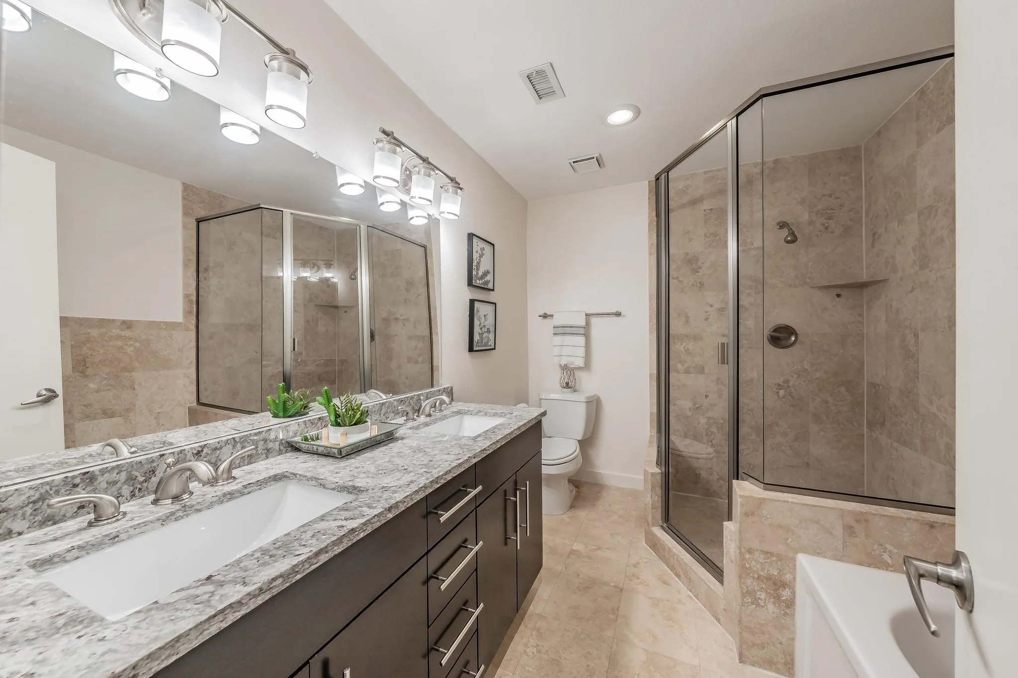 Dual vanity with stone countertop, tile flooring, and a glass-enclosed shower featuring tile surround